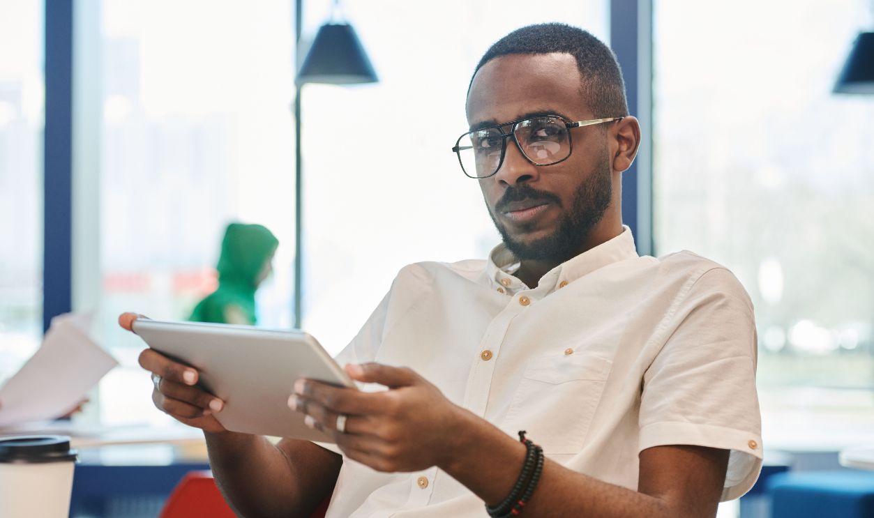 Man sitting indoors using a tablet, wearing eyeglasses