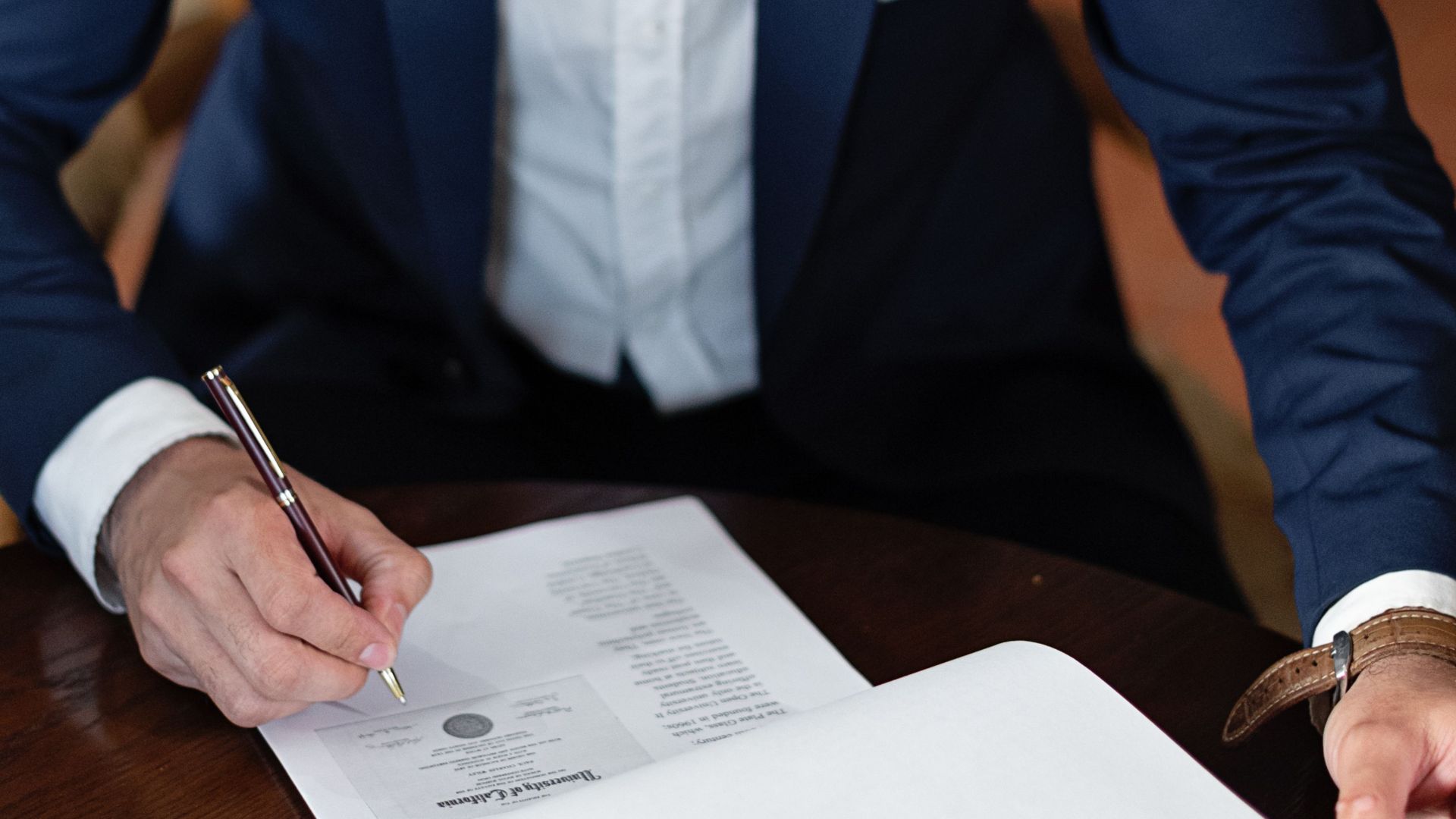 A professional individual signs legal documents at a desk in an office setting.