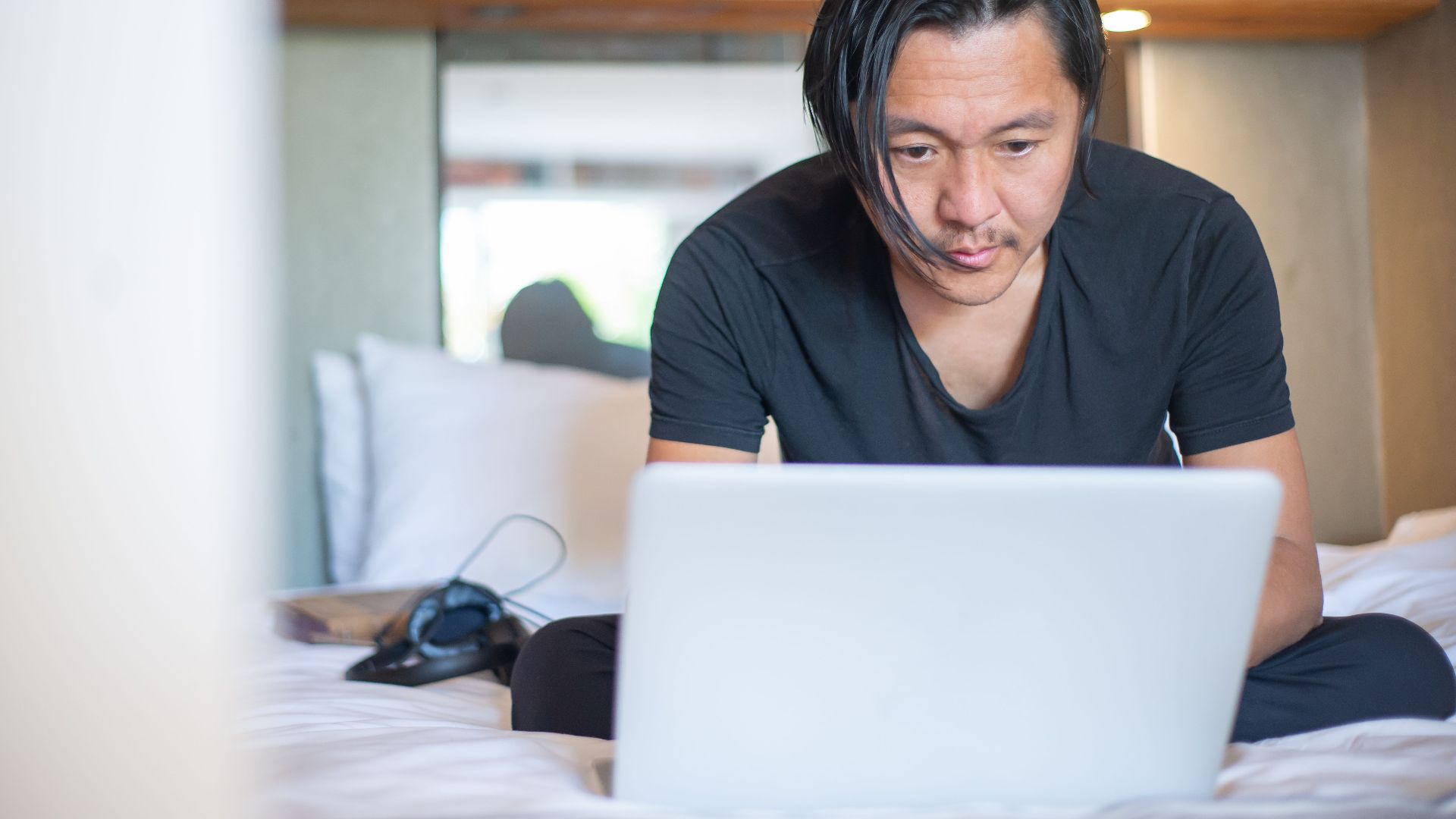 An Asian man working from home on a laptop, focusing on his digital tasks in a cozy indoor setting.