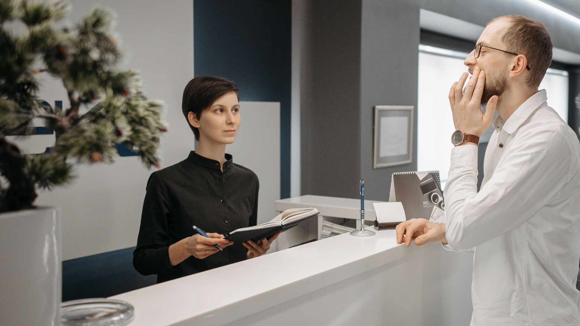 A receptionist assists a patient with a toothache at a dental clinic's front desk.