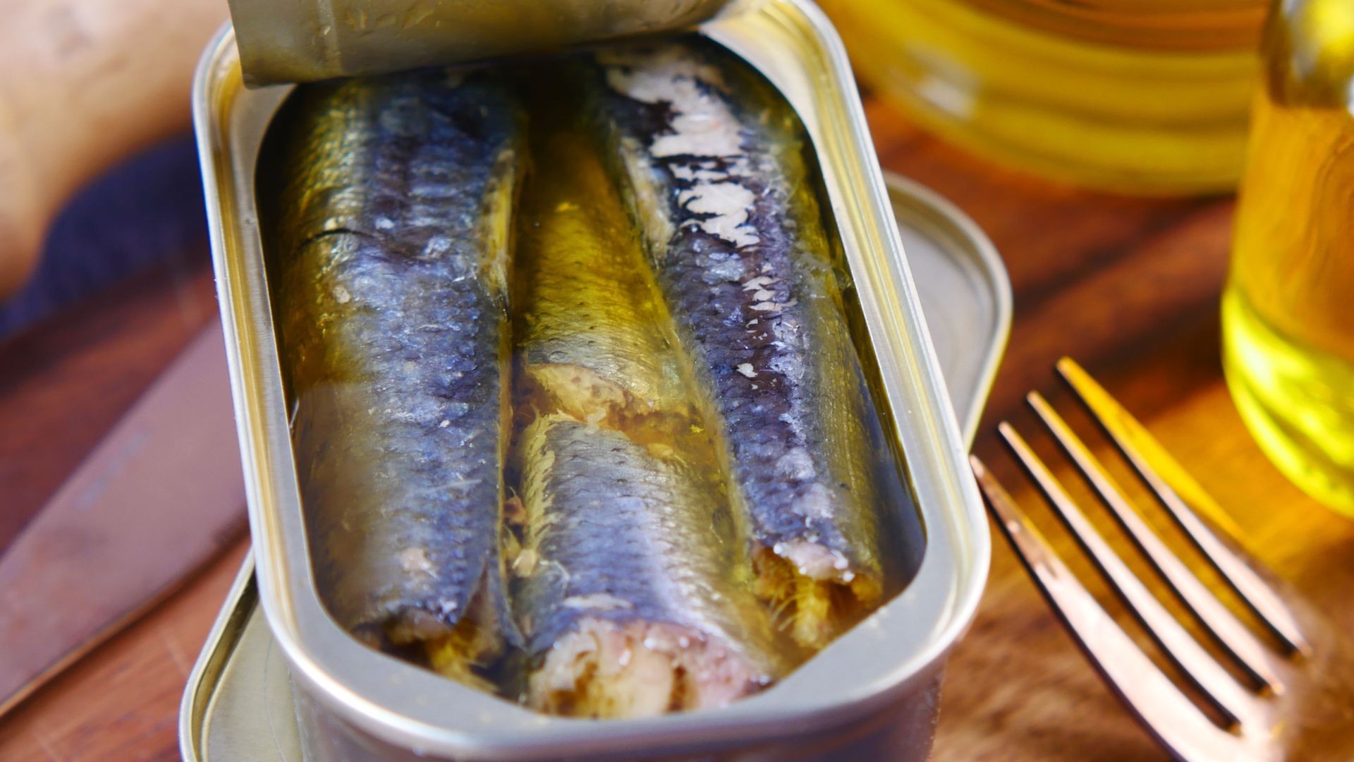 Close-up of canned sardines in olive oil with a fork on a wooden surface.