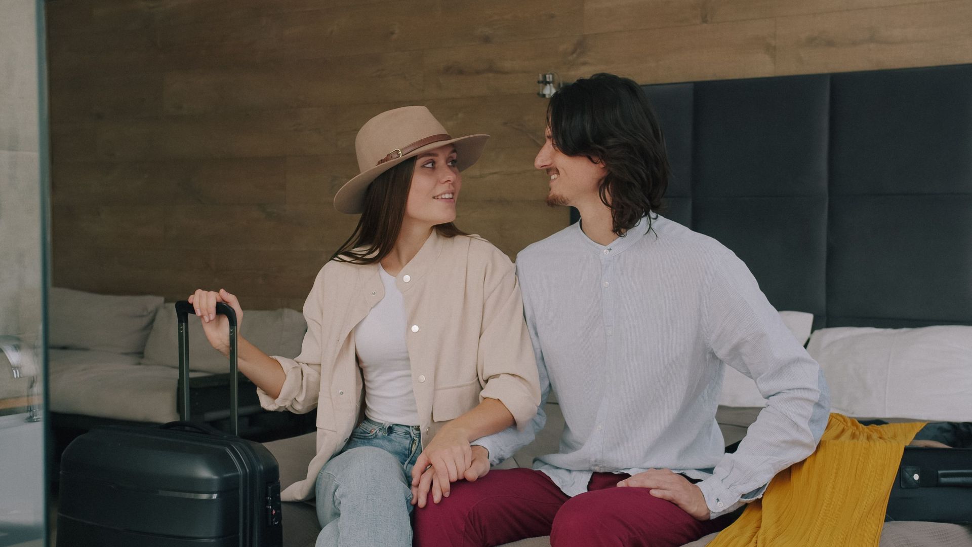 Couple enjoying a moment on a hotel bed, preparing for travel with luggage.
