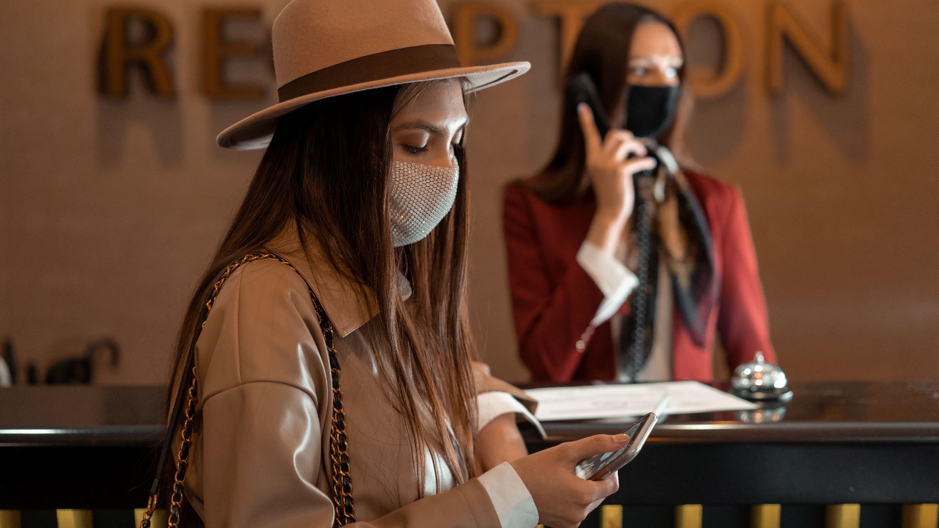Woman wearing a mask checking her phone at a hotel reception during COVID-19.