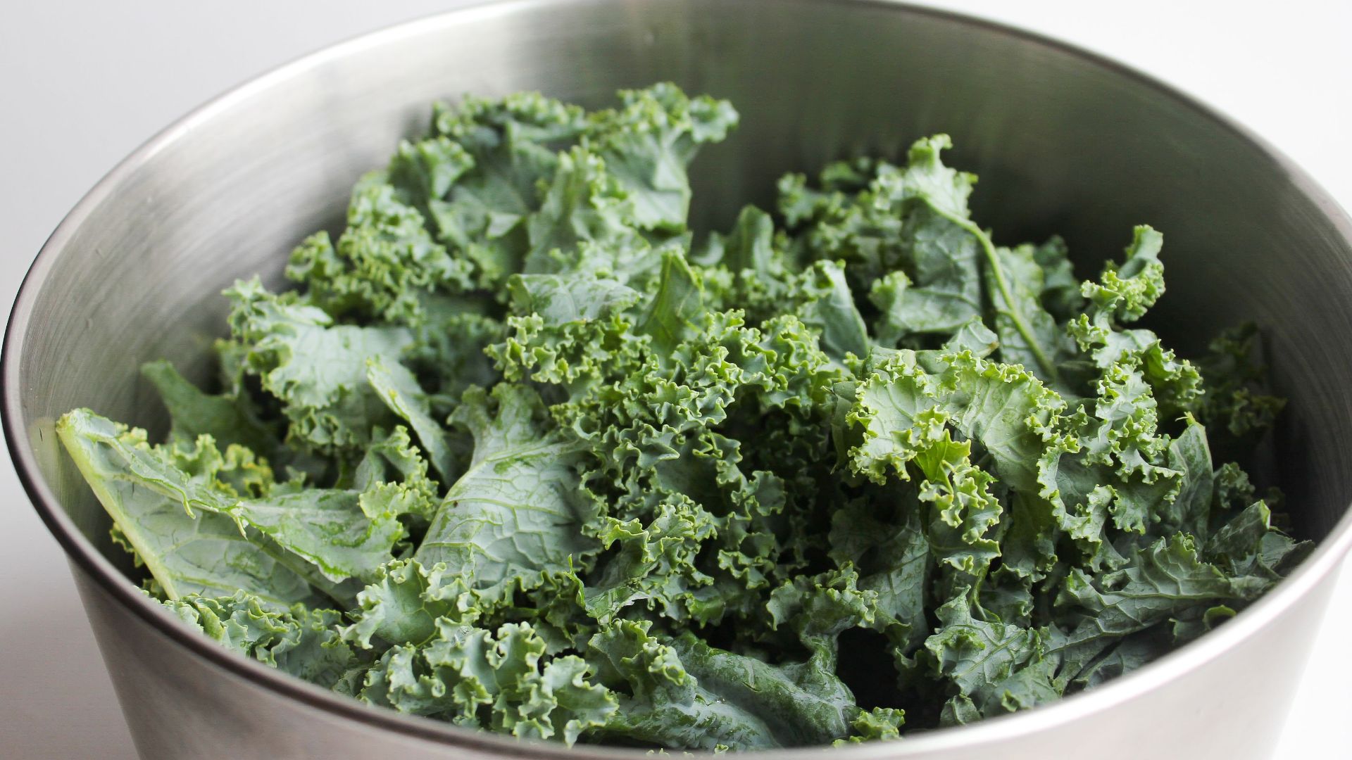 Healthy fresh kale leaves in a stainless steel bowl, perfect for salads and healthy meals.