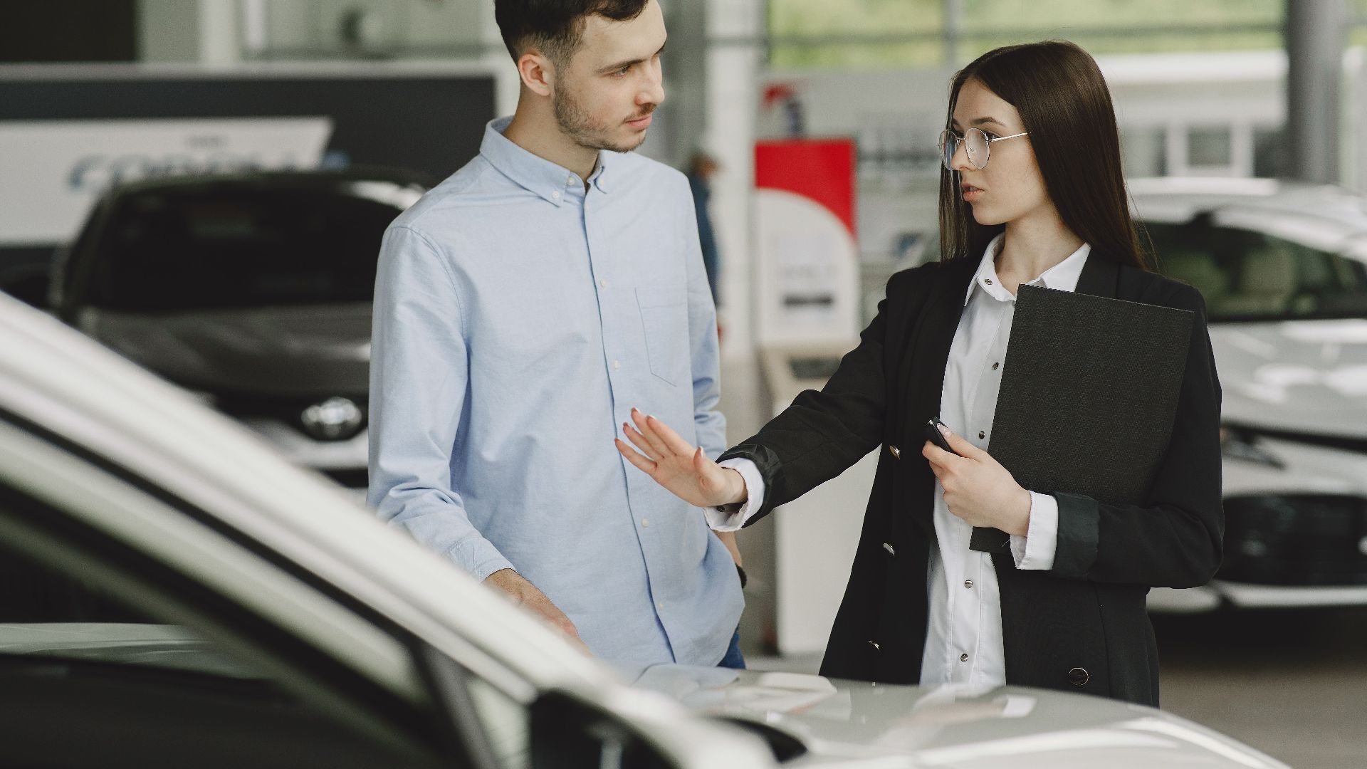 A salesperson and customer discussing car features in a dealership setting.