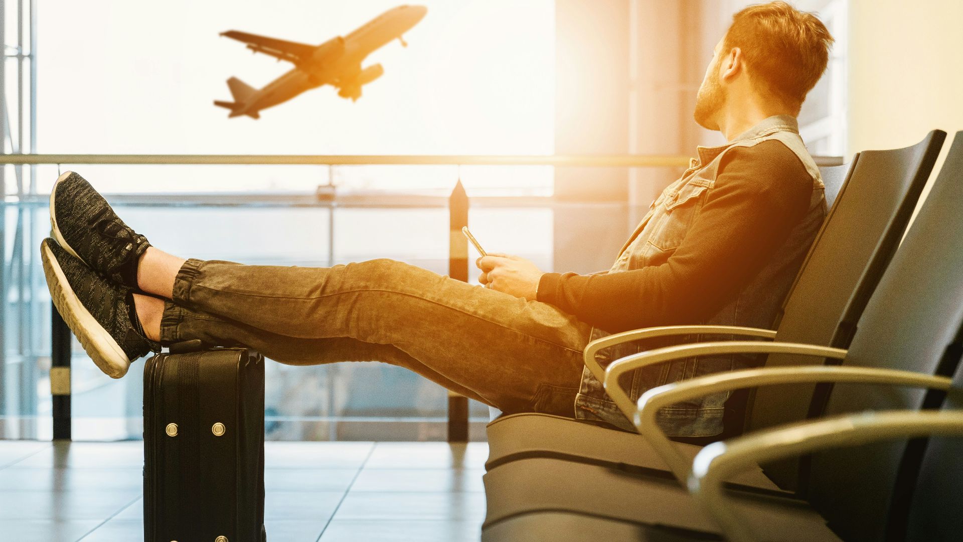 man sitting on gang chair with feet on luggage looking at airplane