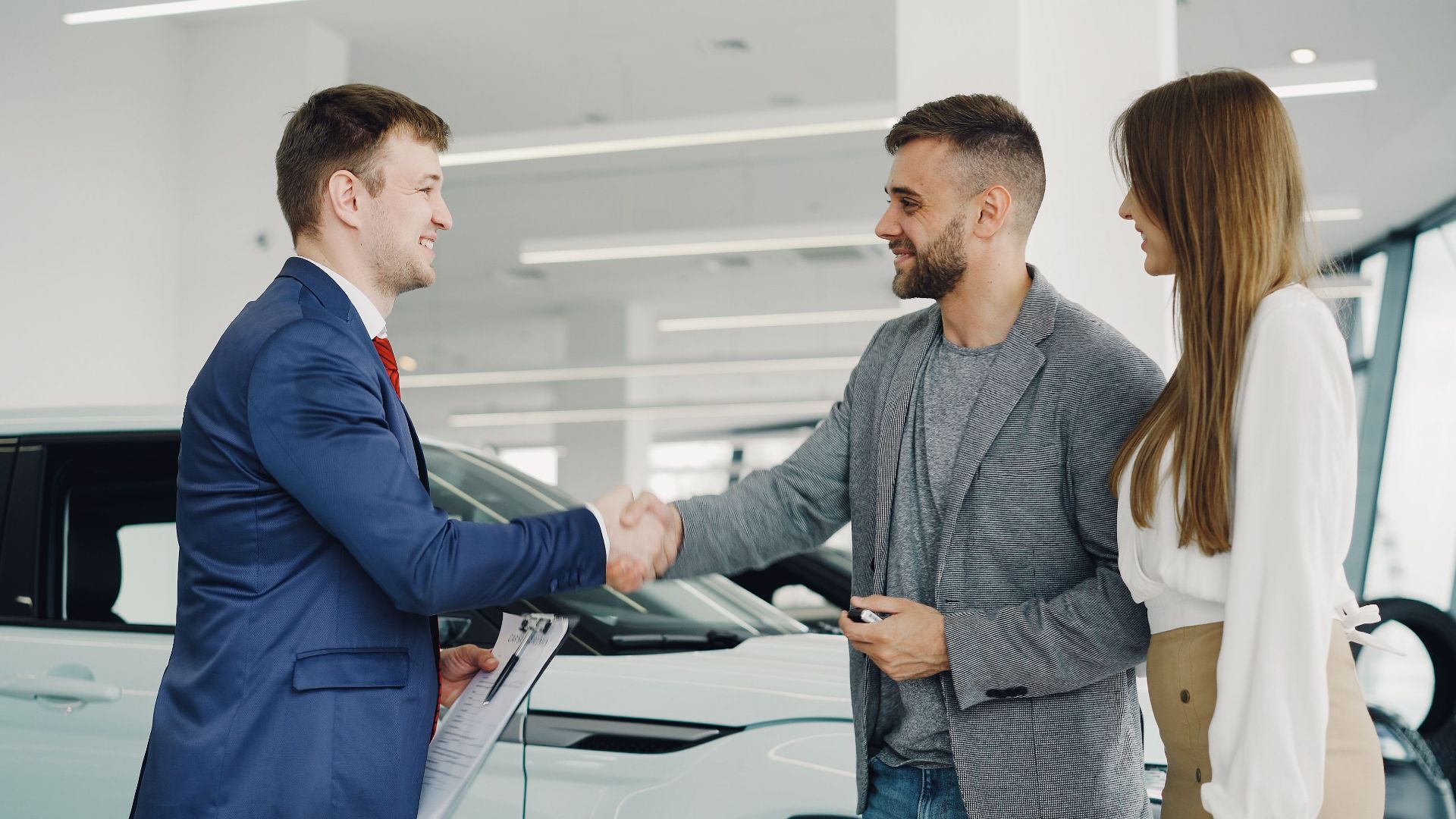 Friendly handshake between a car salesman and customers in a modern car showroom.