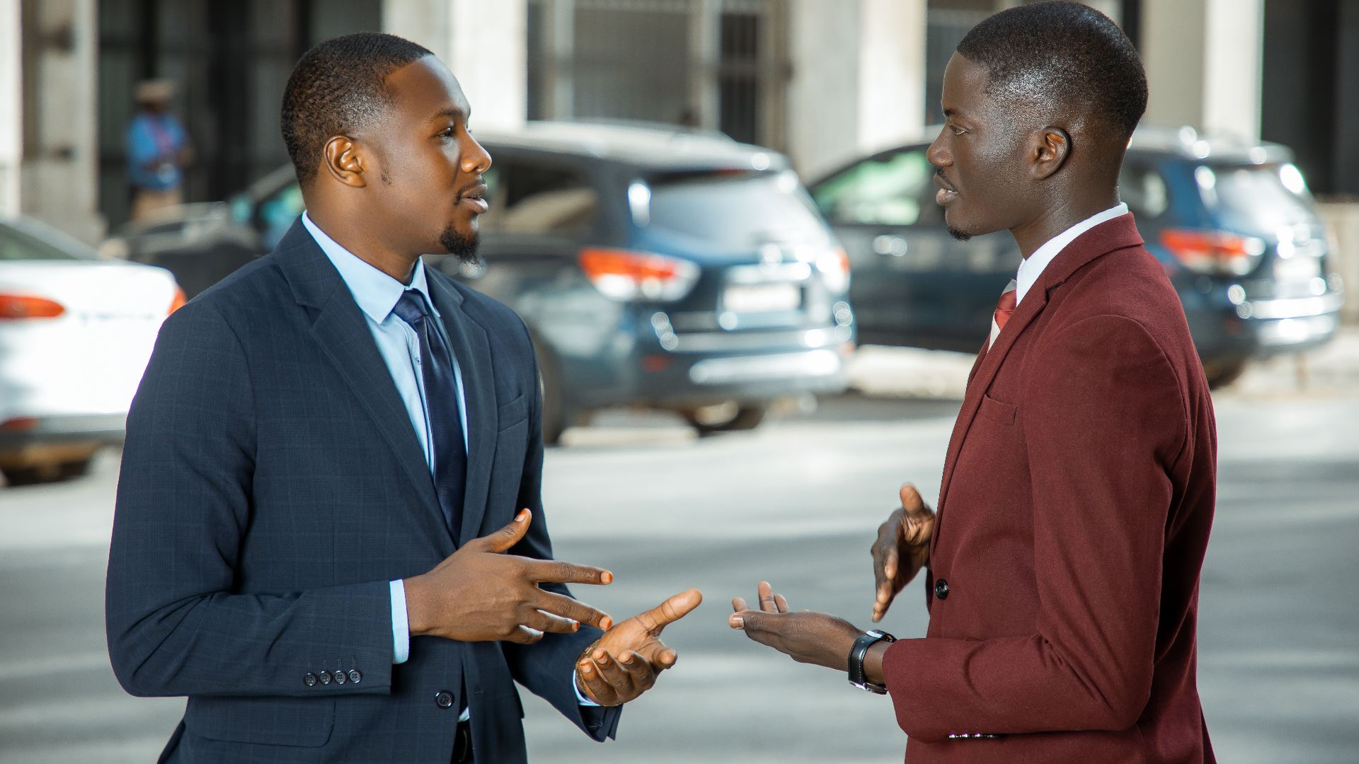 Two African businessmen in formal suits have a discussion on a city street in Dakar, Senegal.
