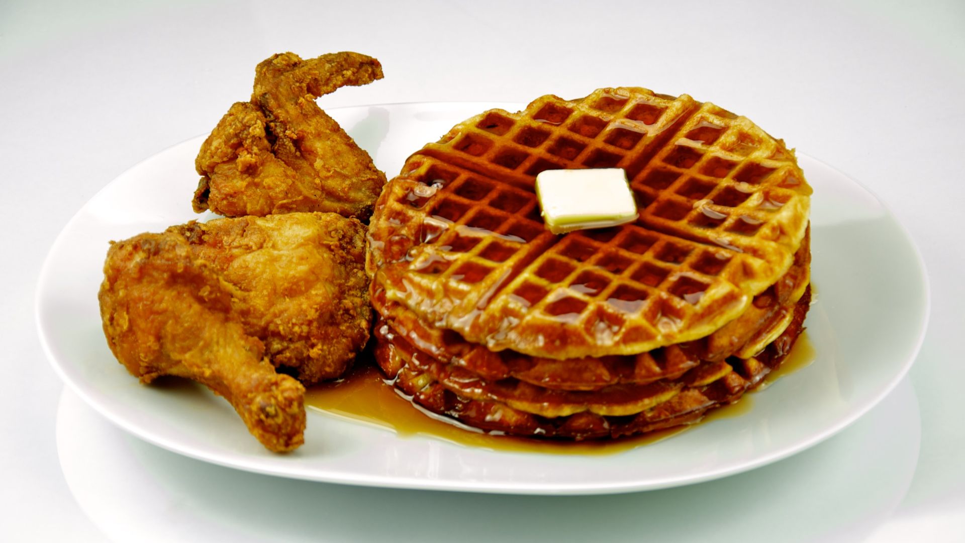 Fried chicken and waffles with maple syrup and butter on a white plate and shot on a white background.