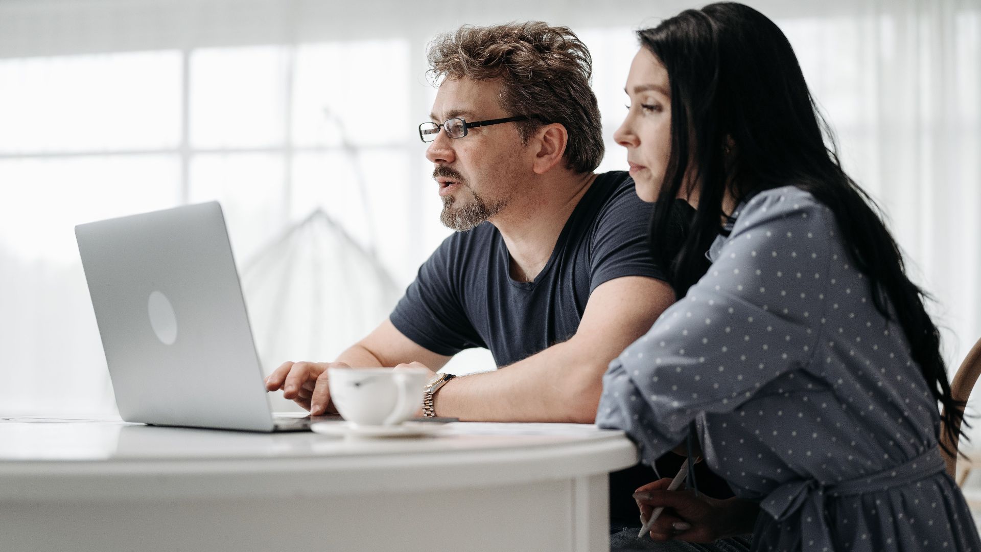 A couple uses a laptop at home in a bright and cozy setting, collaborating closely.
