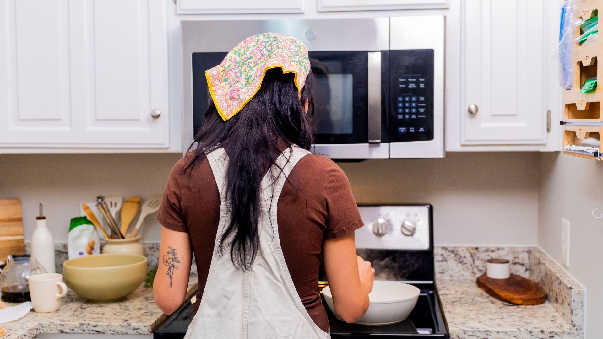 Rear view of a woman cooking in a modern kitchen with white cabinets and granite countertops.
