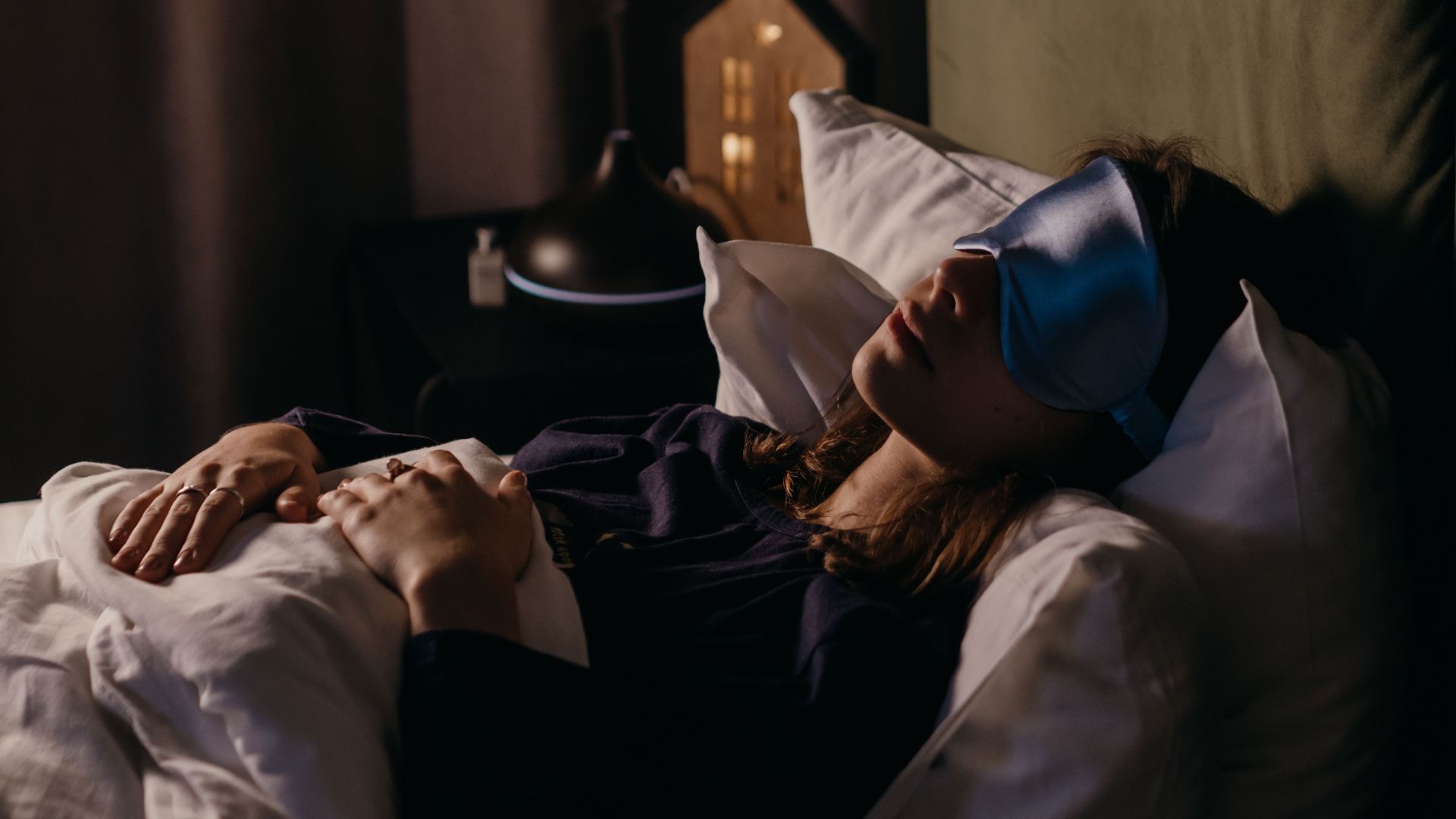 A woman resting with a sleep mask in a calm bedroom setting, creating a serene and cozy atmosphere.