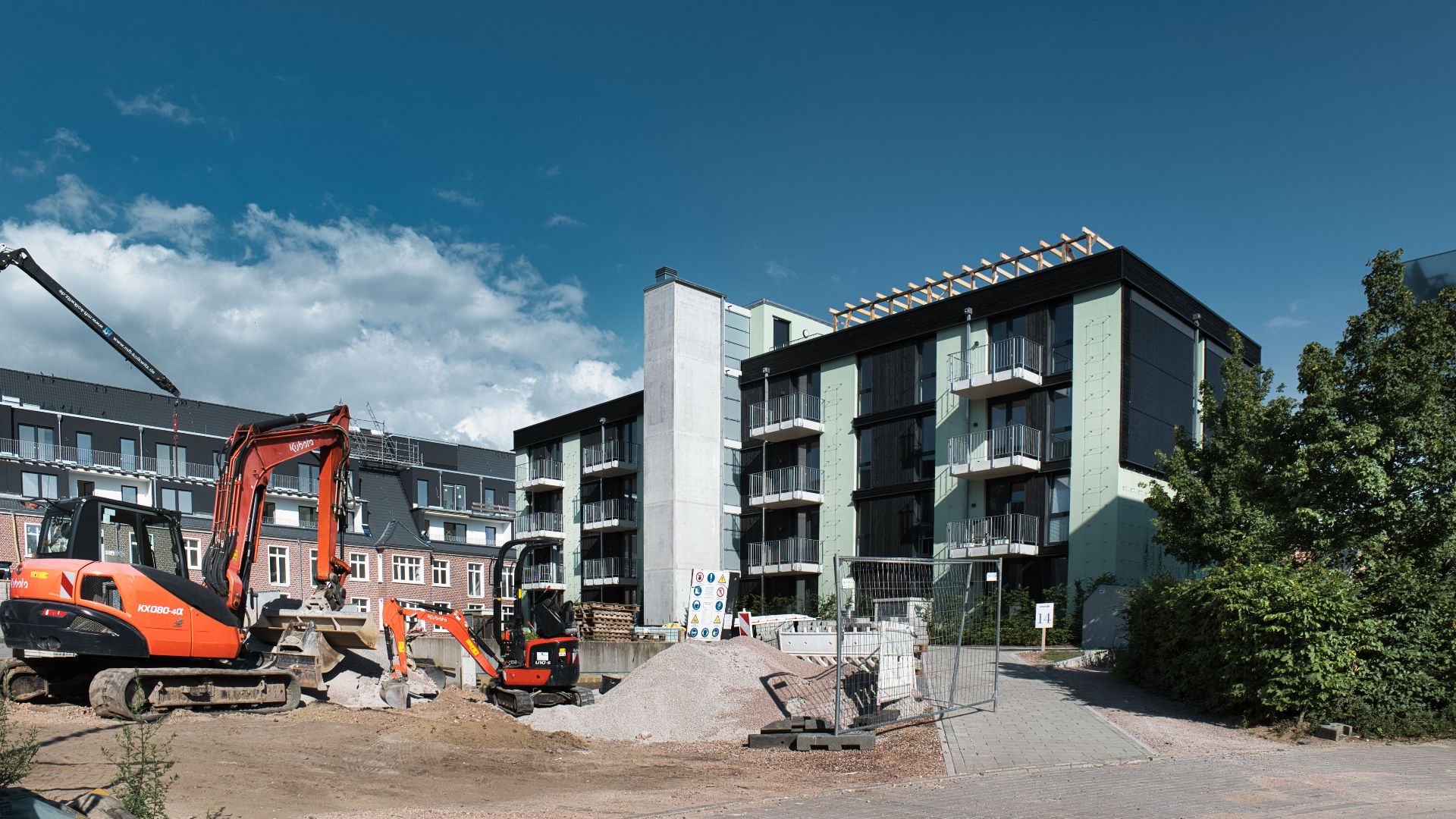 Active construction site with machinery next to modern apartments under blue sky.