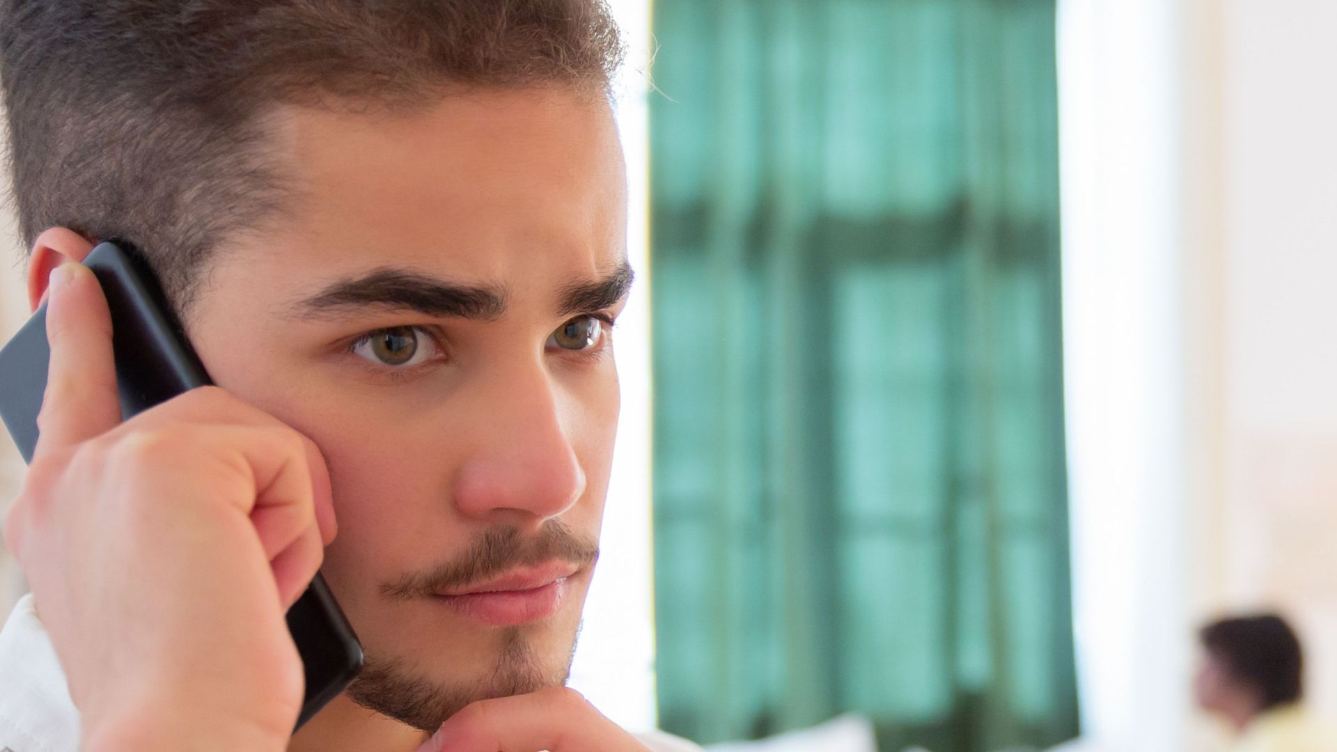 Man engaged in phone conversation in a bright, cozy bedroom setting.