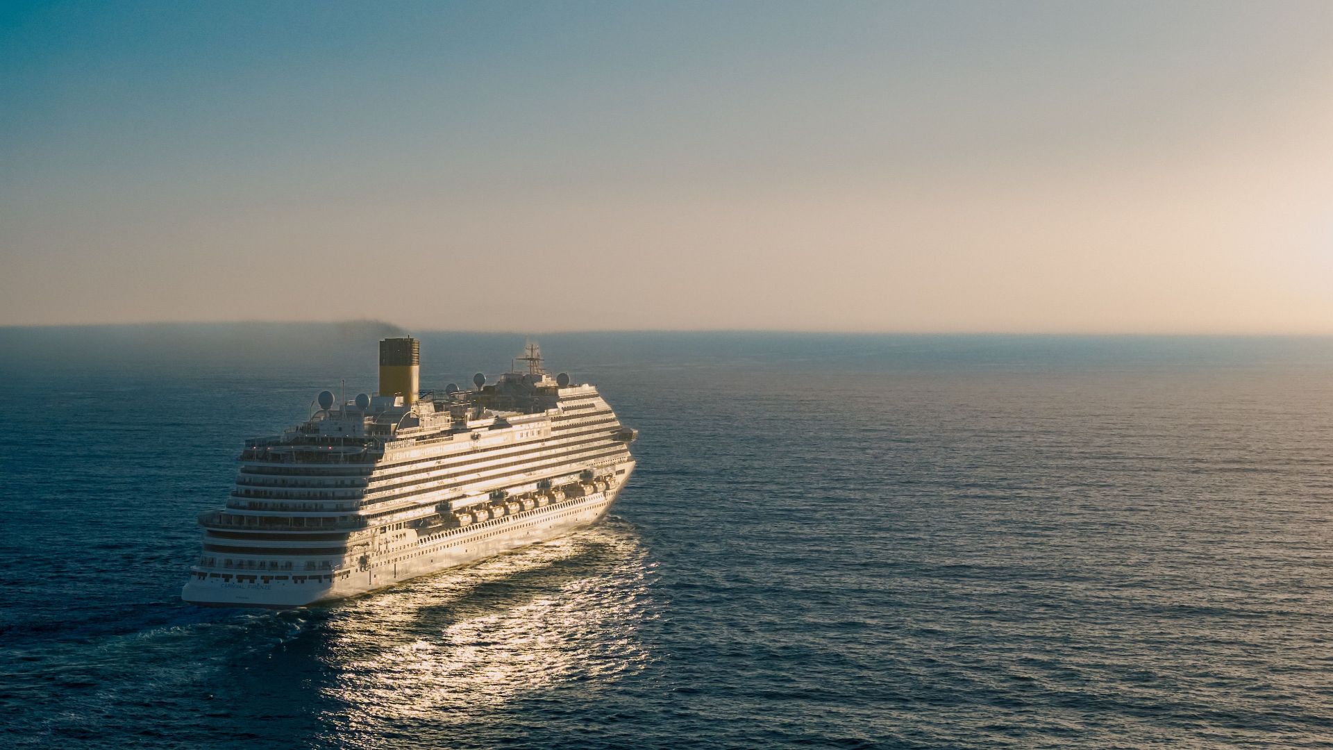 A cruise ship gracefully sails across the ocean at sunset, creating a tranquil scene.
