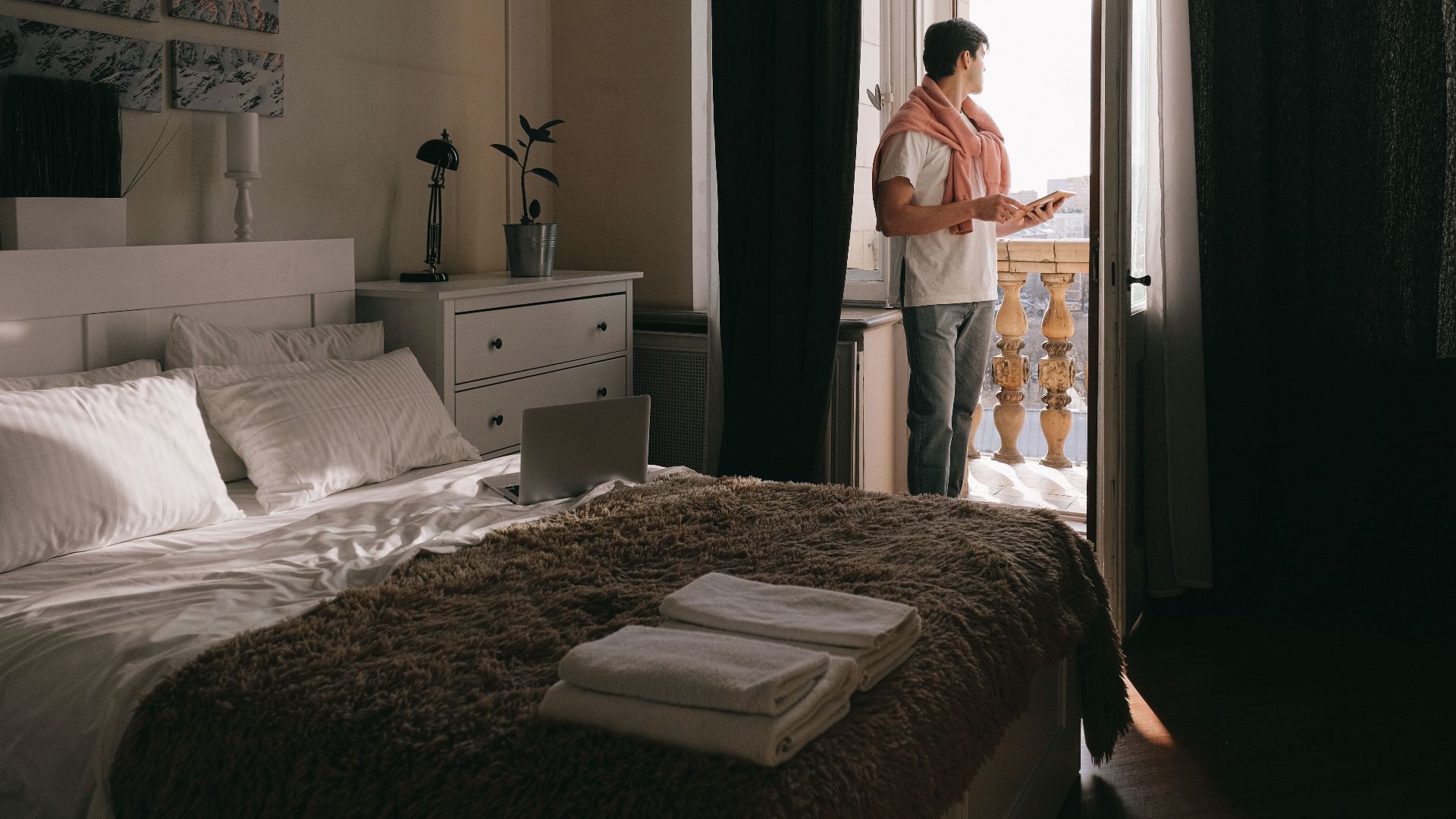A man stands on a bedroom balcony using a tablet, capturing a moment of relaxation and contemplation.