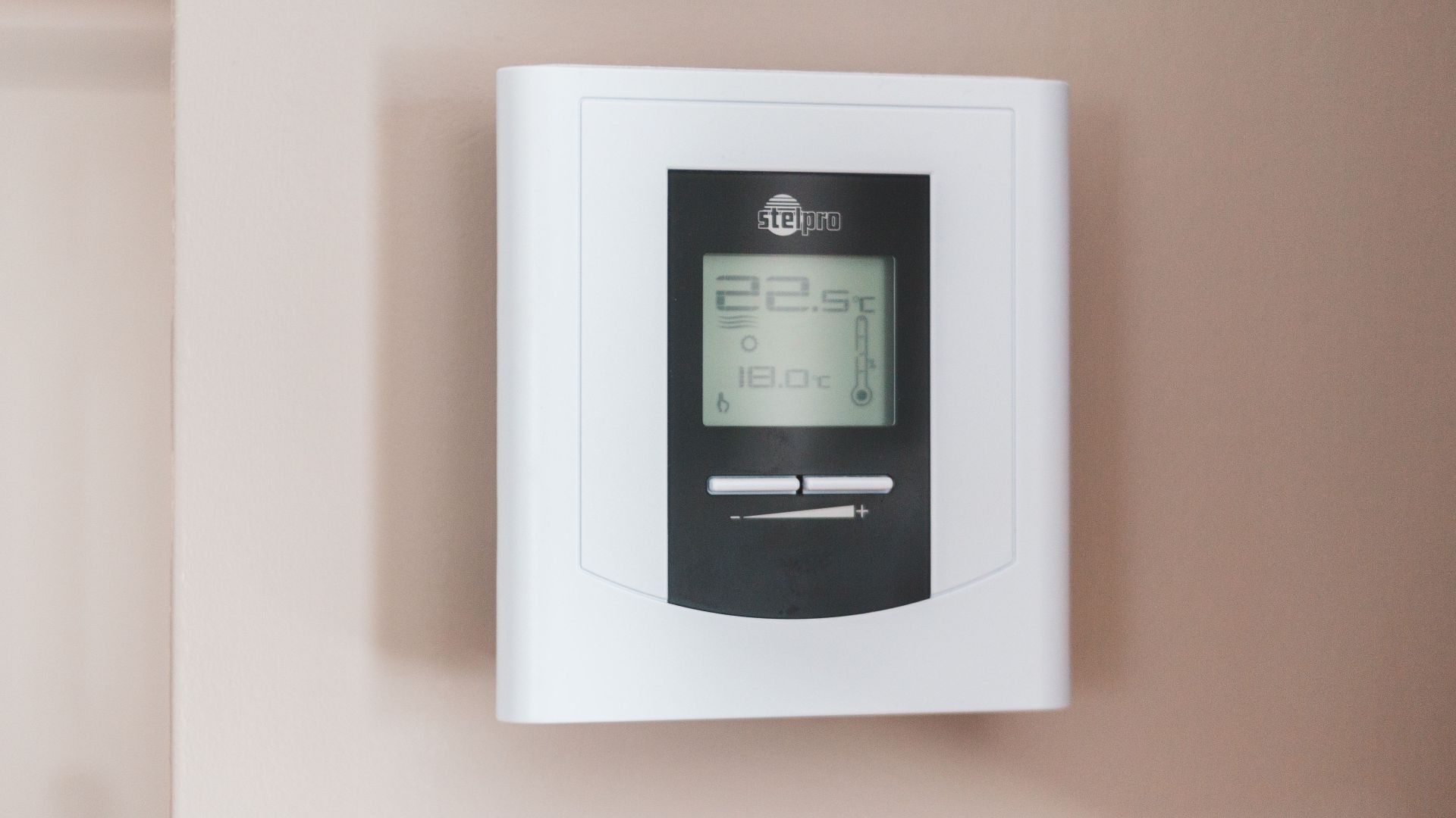 Close-up of a modern digital thermostat mounted on a wall, displaying temperature settings in Celsius.