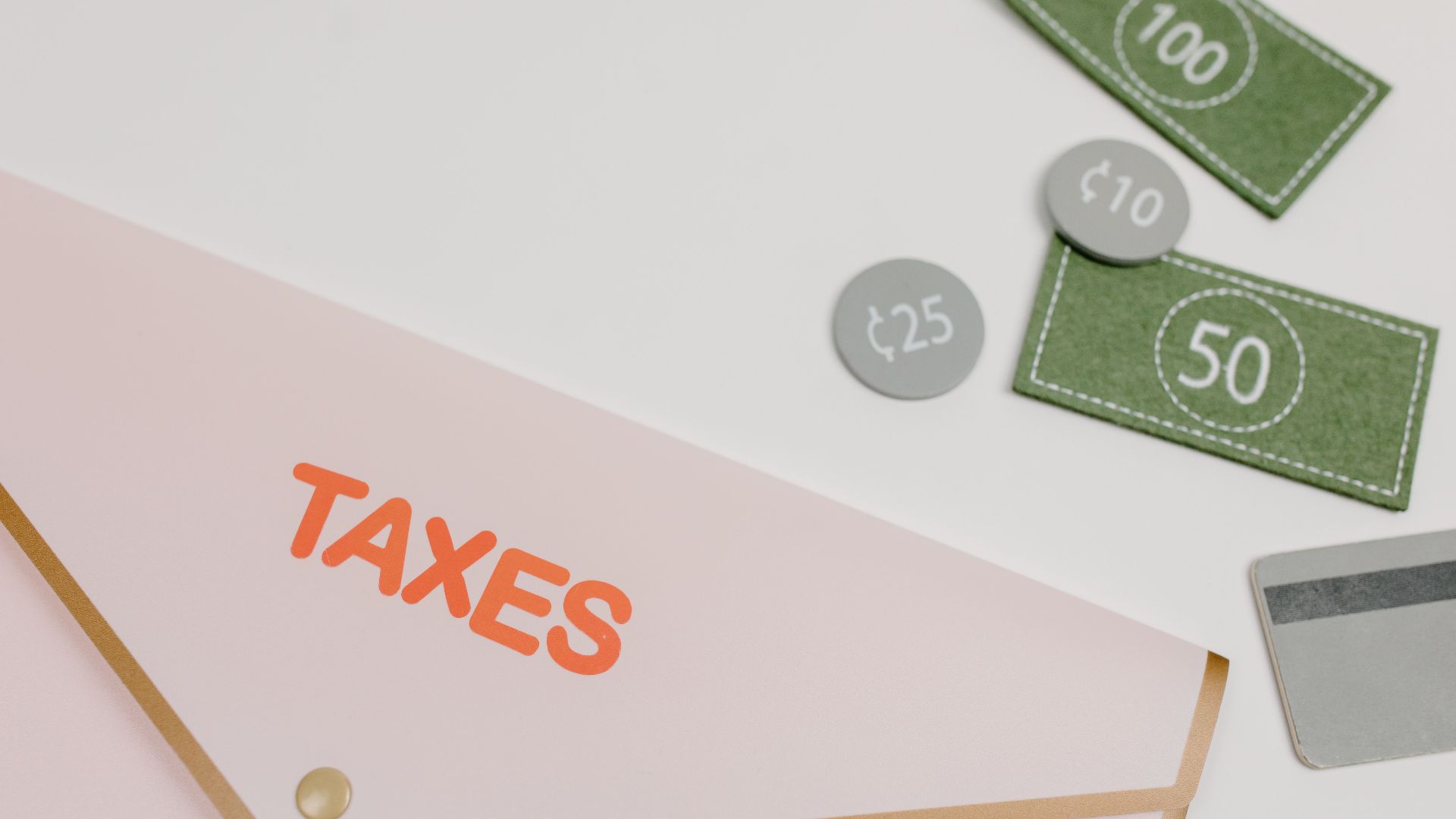 Pink envelope labeled 'TAXES' with play money and card on white background.
