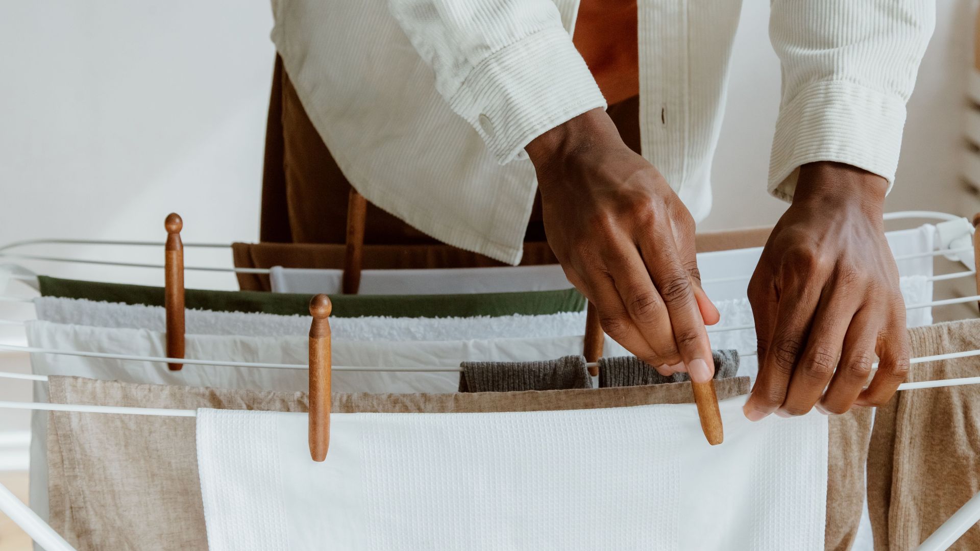 Close-up of a man hanging fresh laundry on a drying rack indoors, emphasizing cleanliness and domestic life.