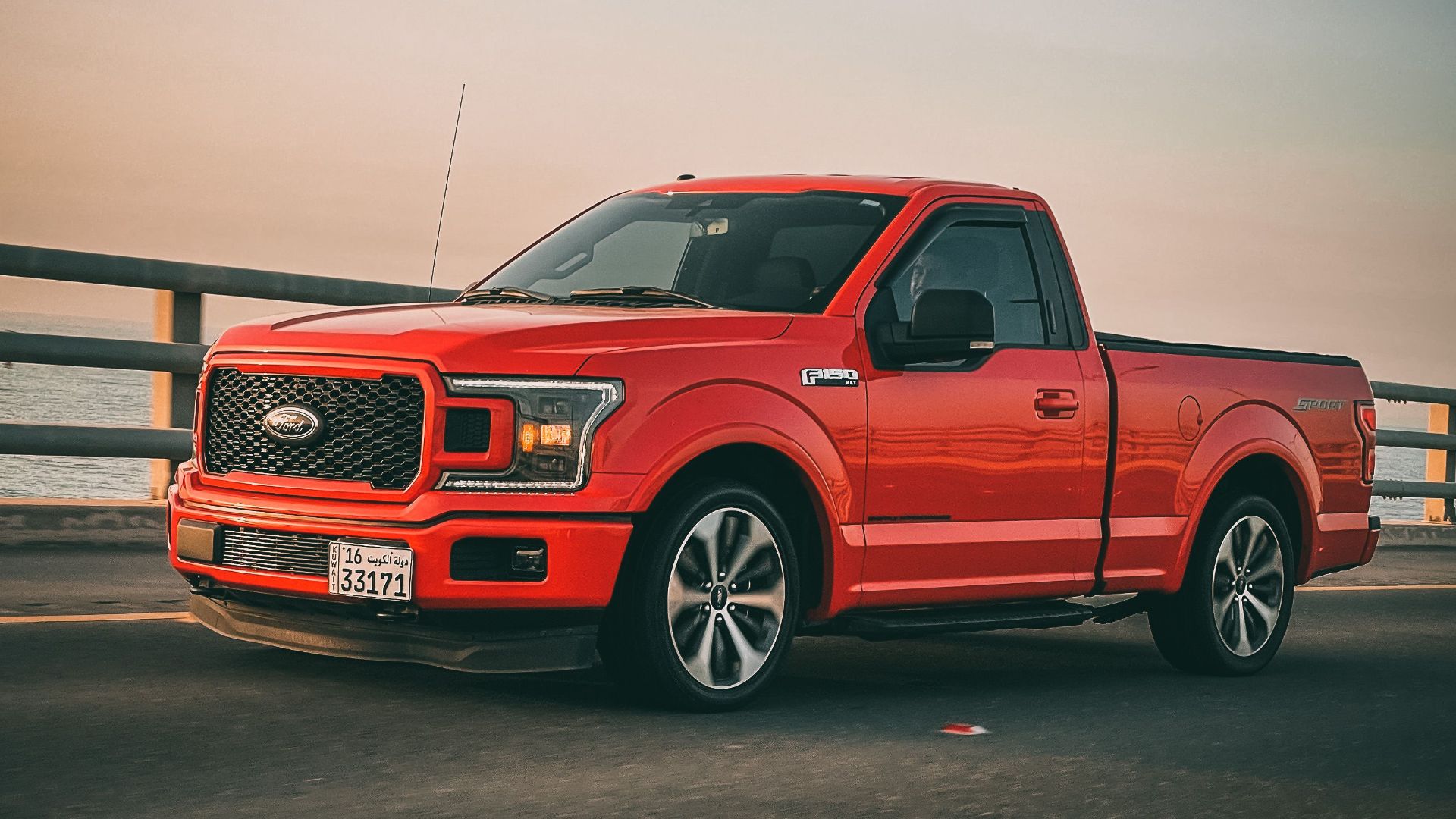 Red Ford F-150 truck driving on a bridge during sunset. Sleek and modern vehicle on the move.