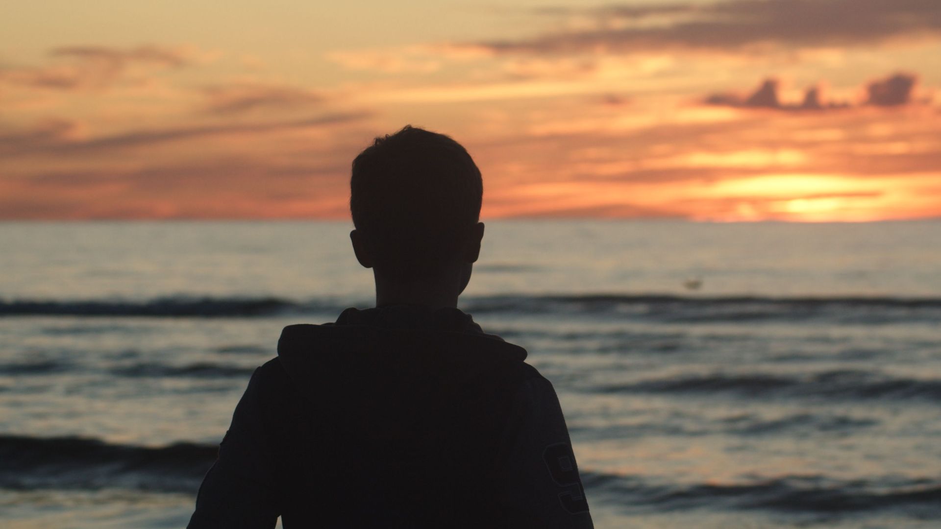 A silhouette of a teenager standing on the beach during a stunning sunset over the ocean.