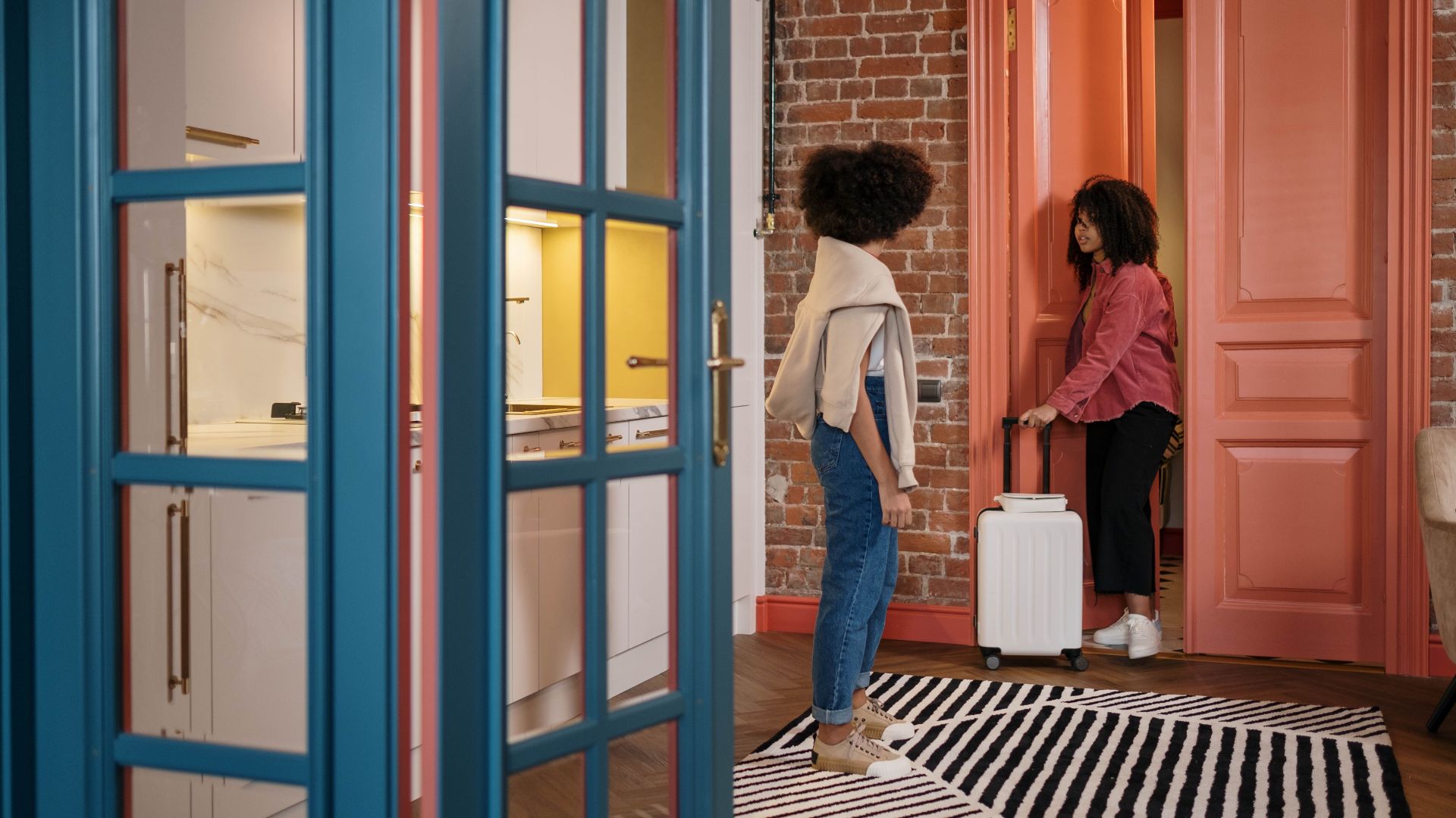 Two women with luggage in a stylish apartment hallway, getting ready to travel.