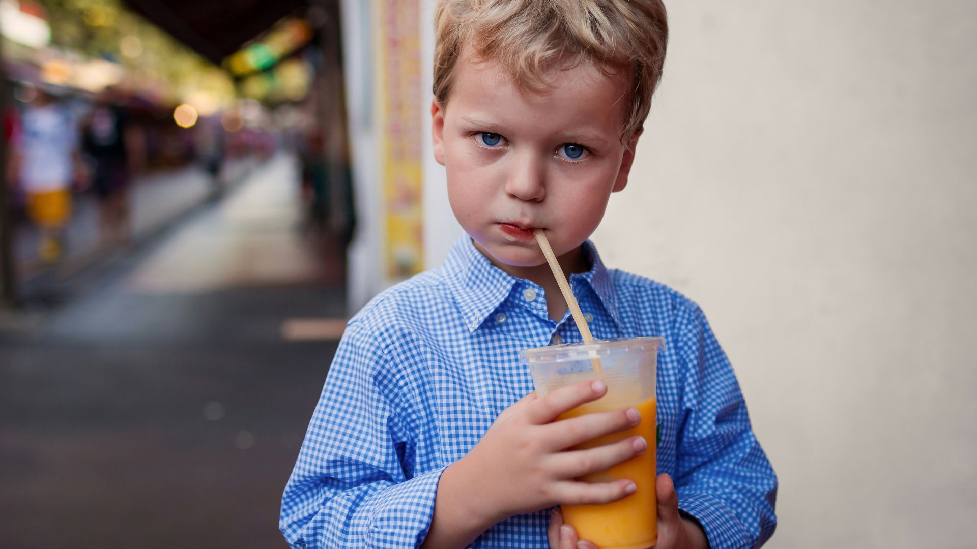 A young boy in a blue shirt drinks orange juice