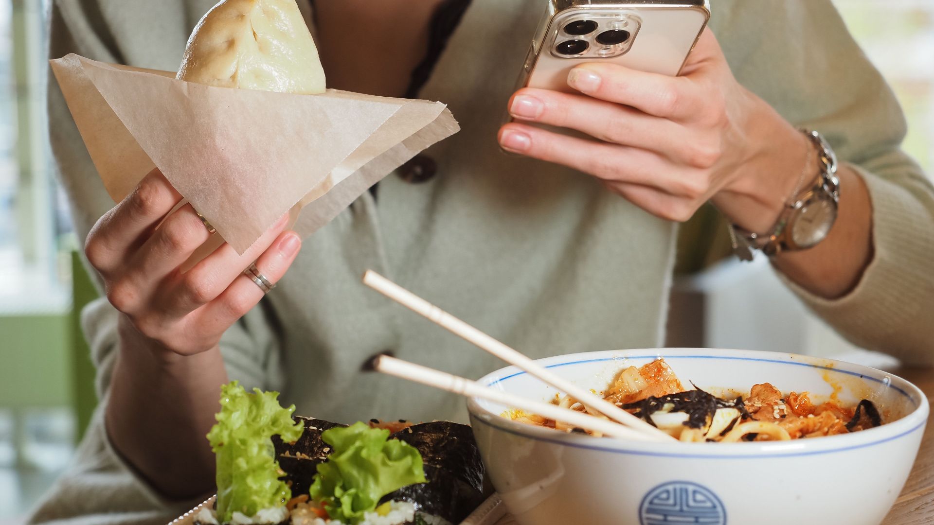 Person enjoying Asian food while using a smartphone at a casual dining setting.