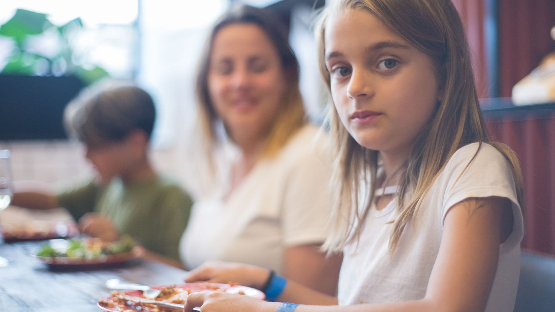 A family enjoying a meal together, focusing on a young girl at the dining table.