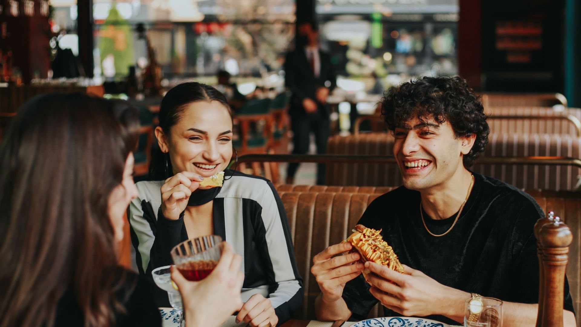 Group of friends laughing and eating at a restaurant, enjoying leisure time.