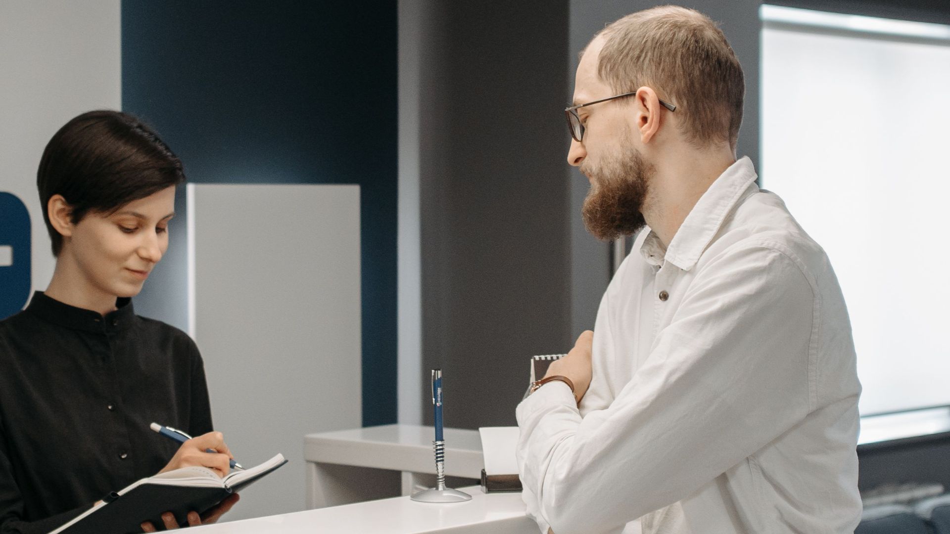 A man consults a receptionist in a modern clinic setting with contemporary design.