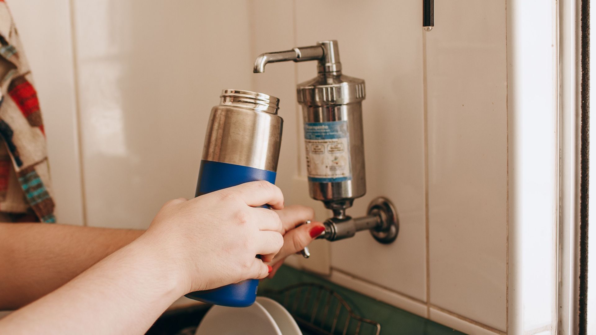Close-up of hands filling a reusable water bottle at an indoor kitchen sink.