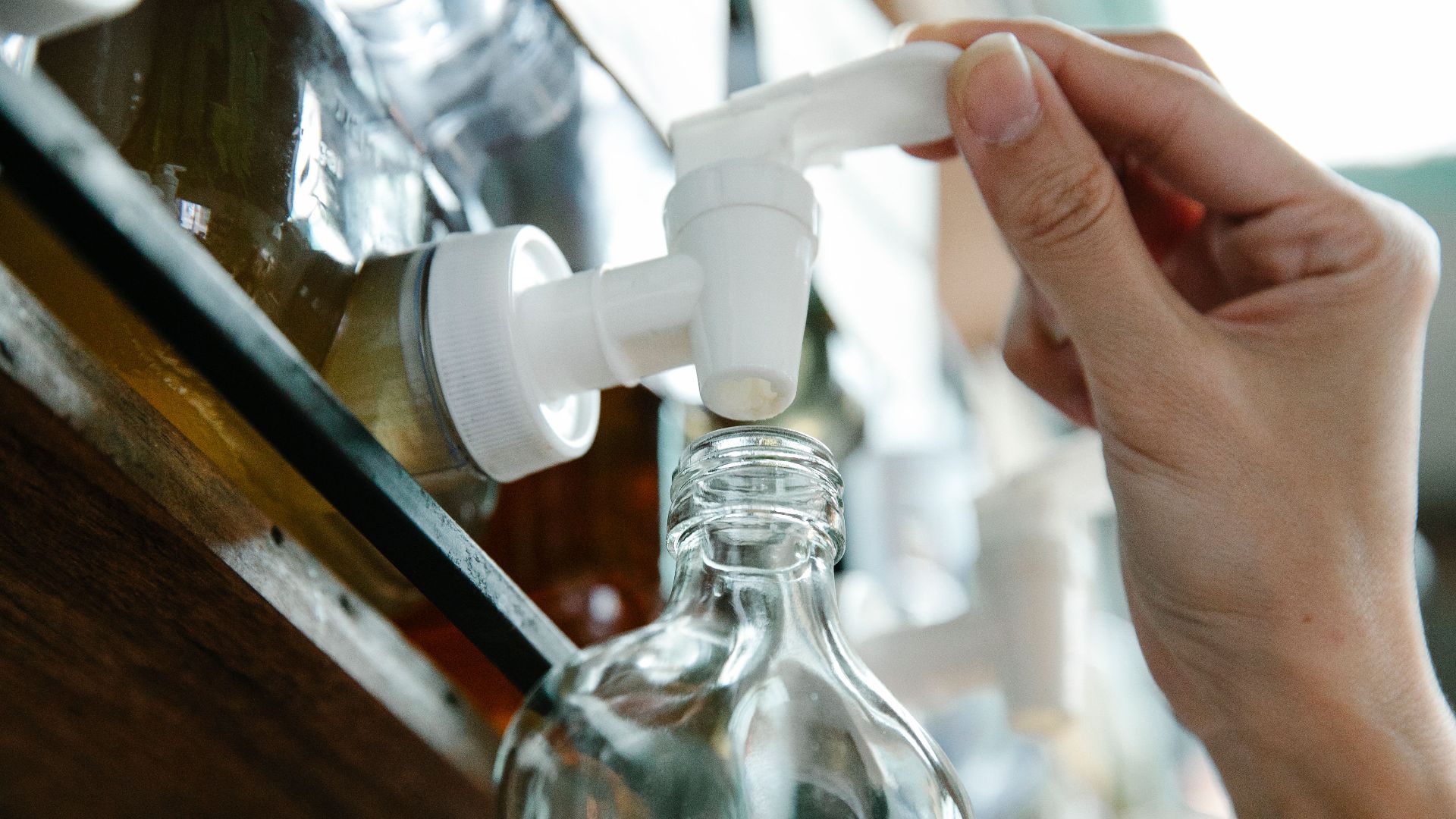 Close-up of a hand refilling a glass bottle from a liquid dispenser with a pump in an eco-friendly setup.