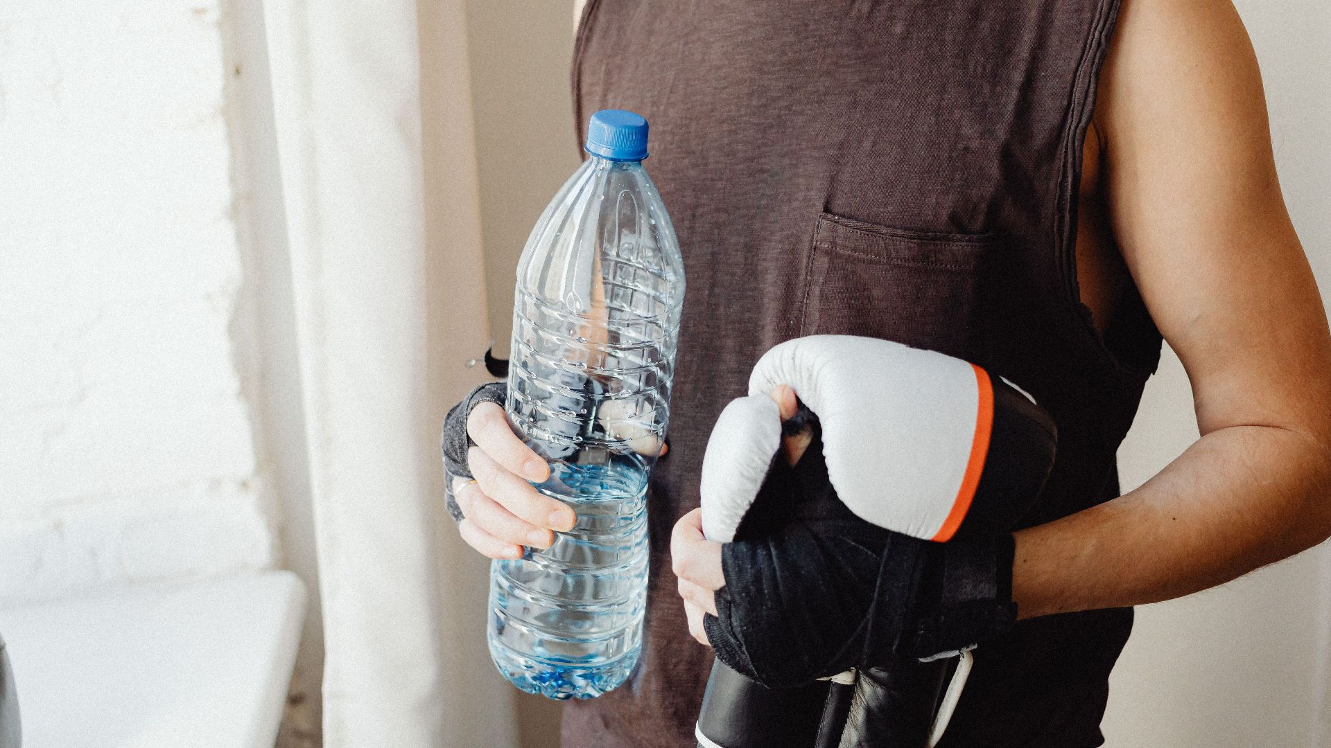 A male boxer holding a water bottle and boxing gloves, representing a healthy lifestyle.