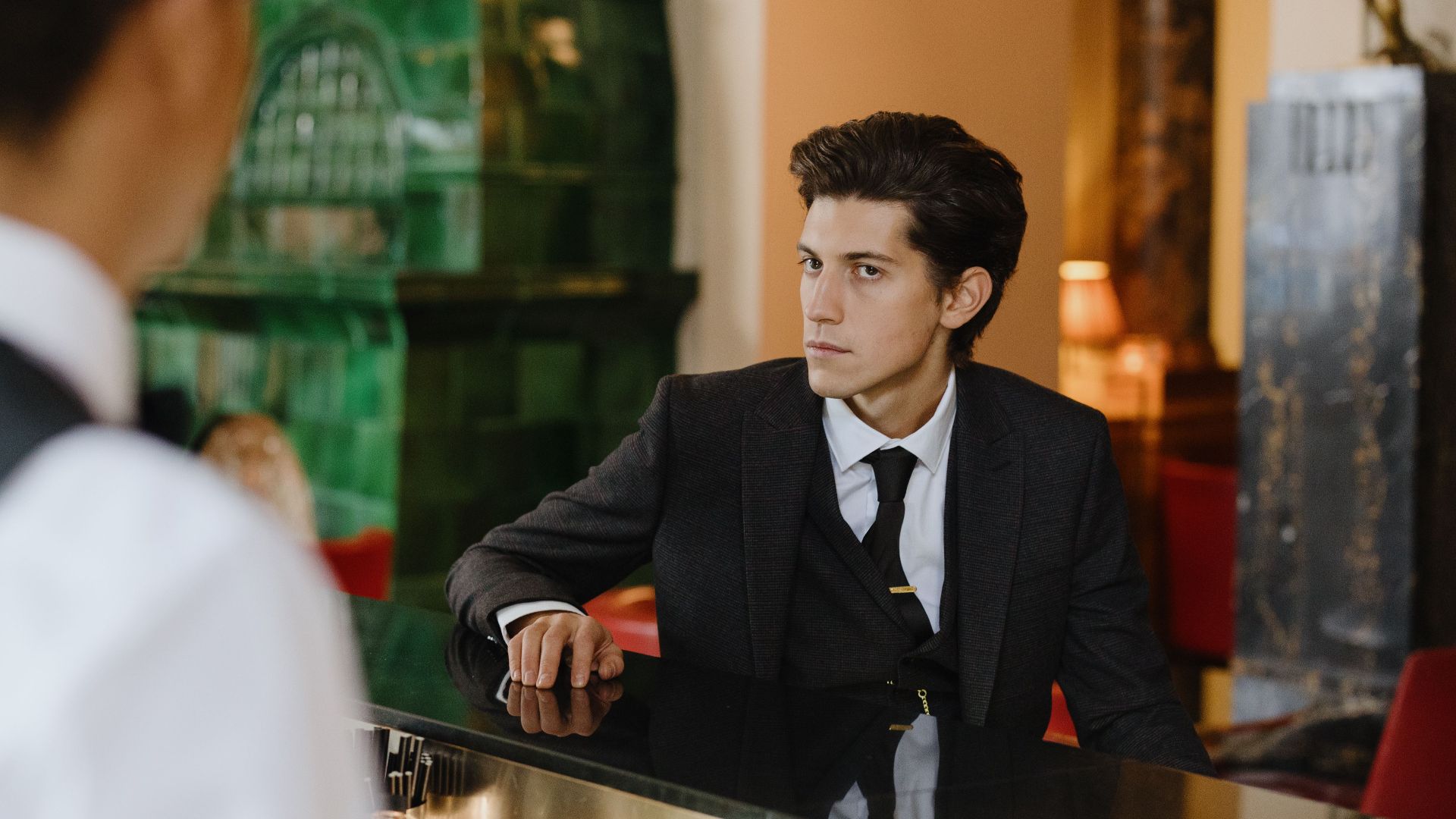 Sophisticated man in a suit sitting at a vintage bar counter indoors, exuding elegance and style.