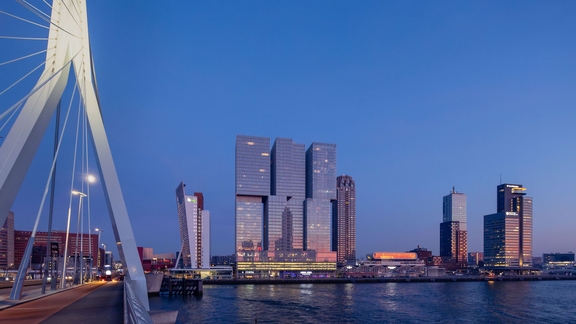 Stunning dusk view of Erasmus Bridge and Rotterdam skyline with modern architecture reflecting in the water.