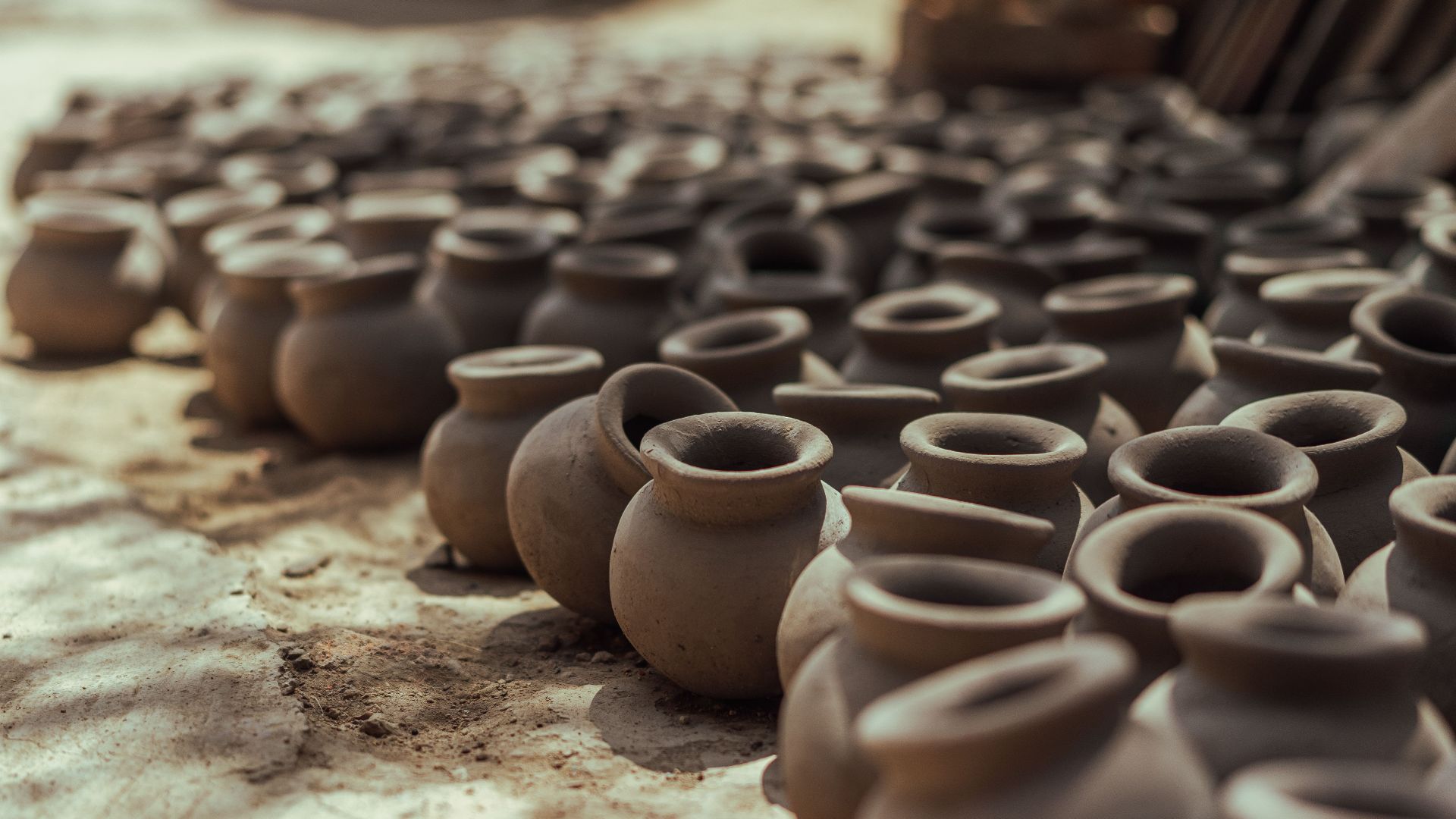 Rows of handmade clay pots drying on the ground under the sun, showcasing traditional pottery techniques.