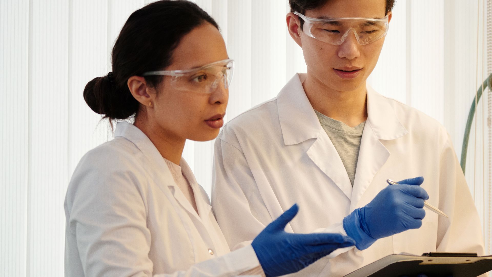 Researchers discussing data in a laboratory setting, wearing safety gear and blue gloves.