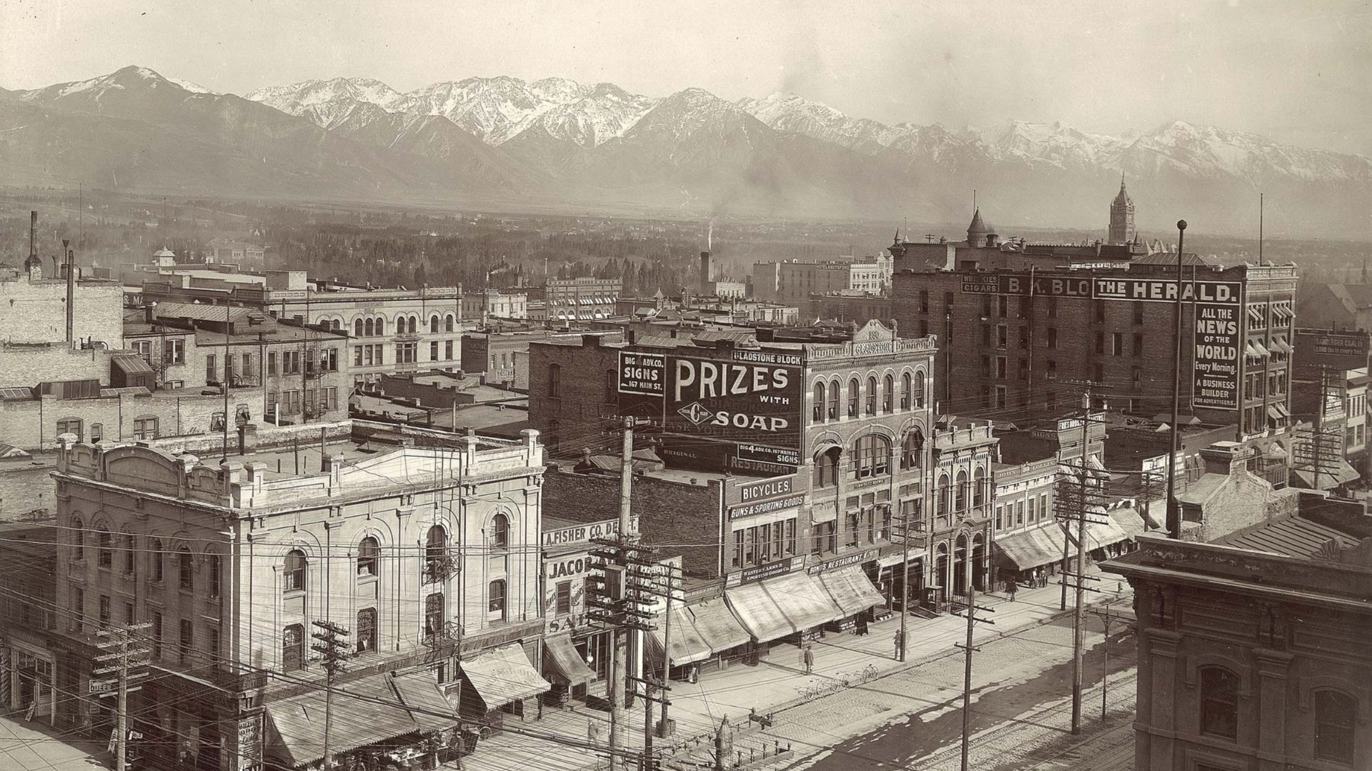 A city street scene of shops, with snow on the ground. Written on the back- Salt Lake City, looking South-East from the McCormick building.