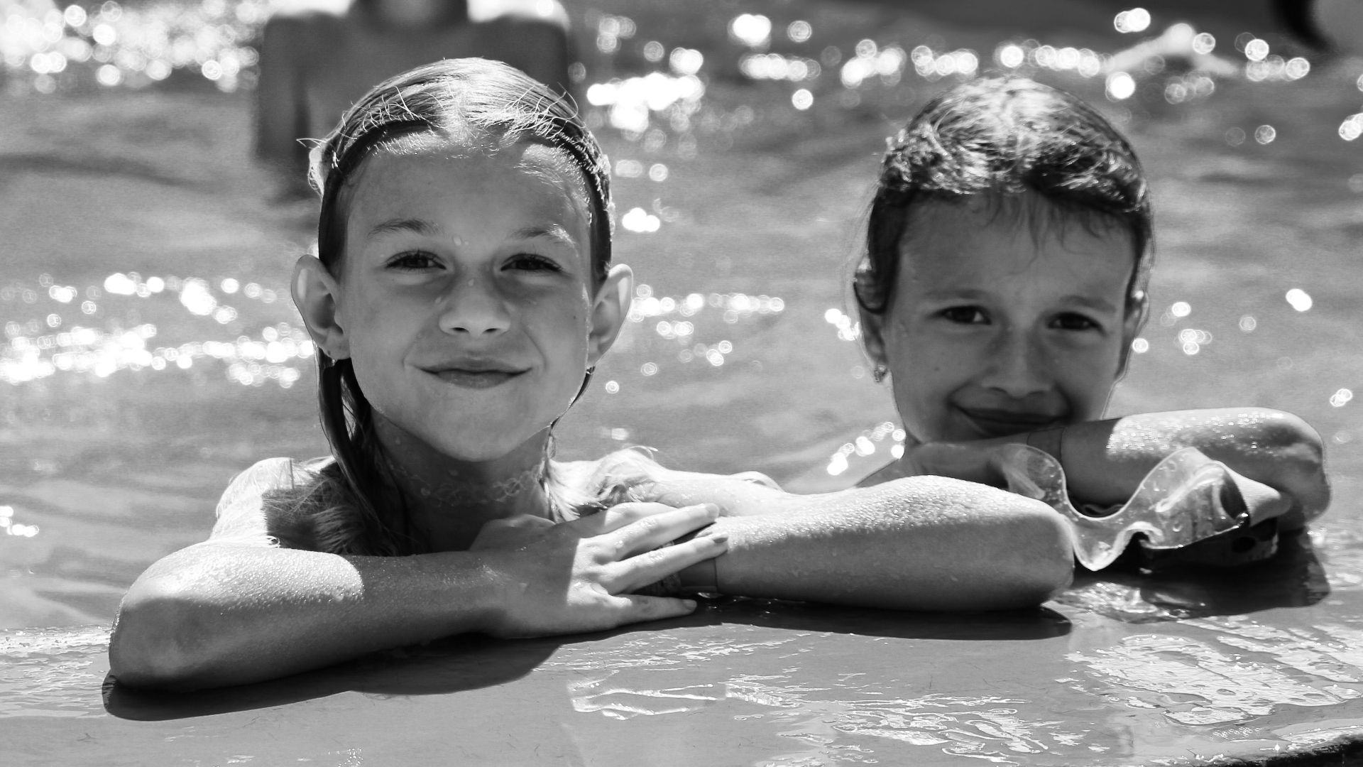 Smiling children at a poolside in a playful black and white summer scene.
