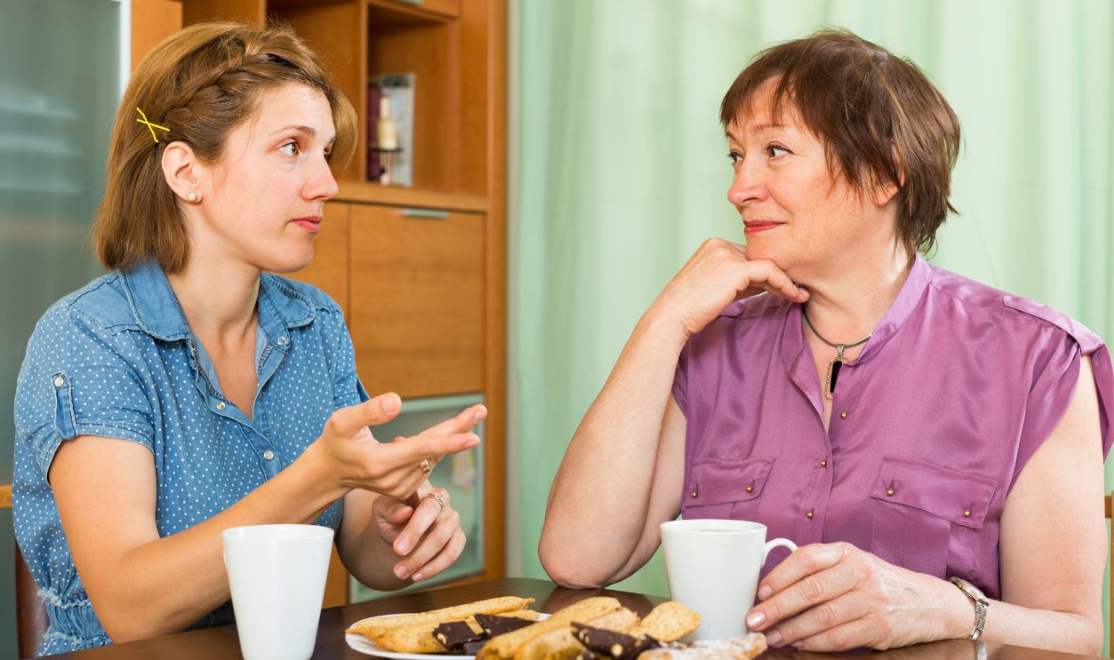 Young girl and her elderly mother having tea-drinking at the table and talking