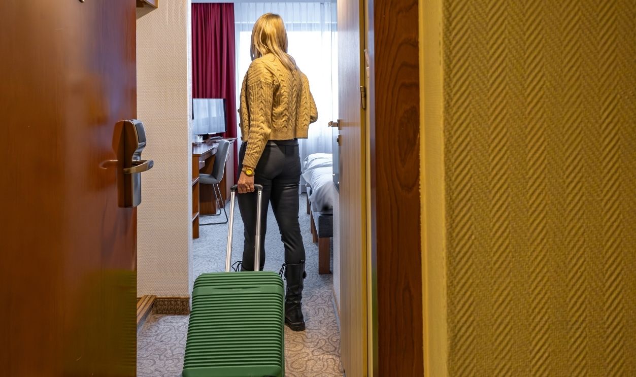 Woman enters a hotel room with a green suitcase, beginning of vacation, accommodation in an apartment, door to a room in a guesthouse