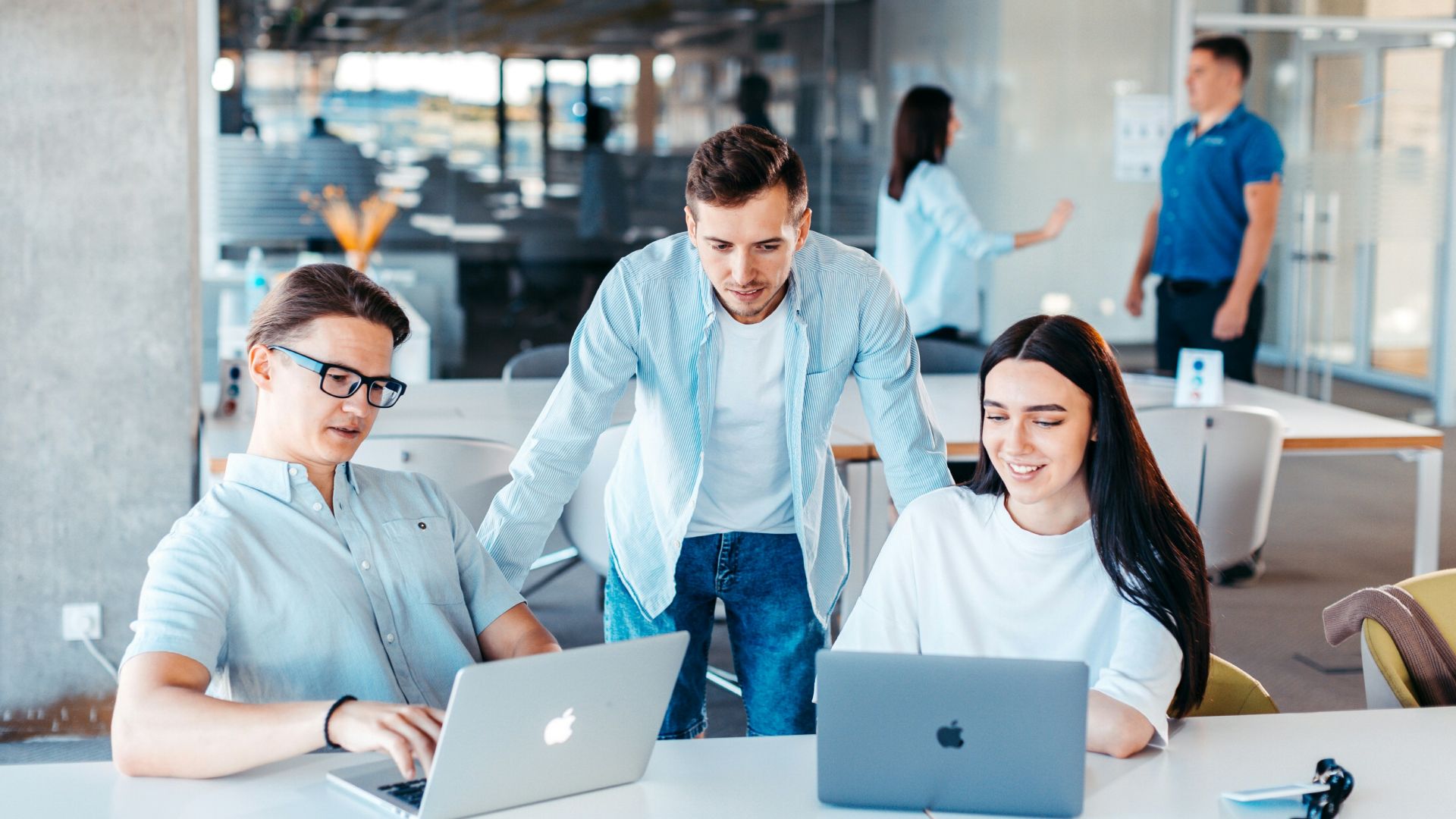 a group of people sitting around a table with laptops