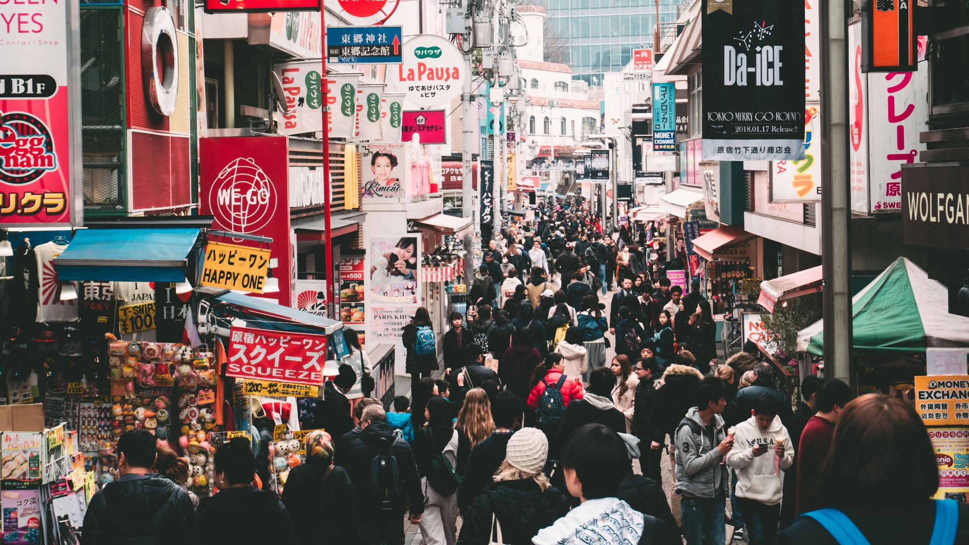 Vibrant daytime street market in Tokyo, crowded with shoppers and colorful signage.