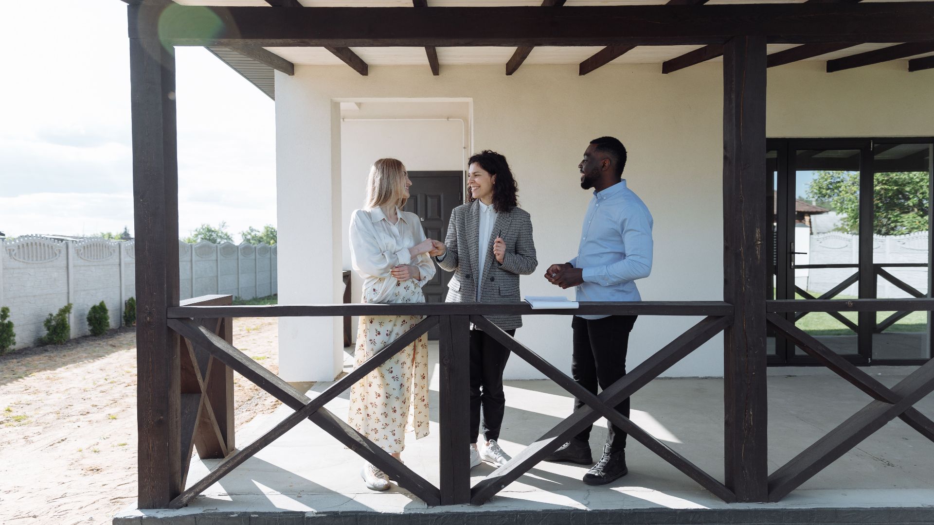 A real estate agent discussing property details with clients on a sunny porch.