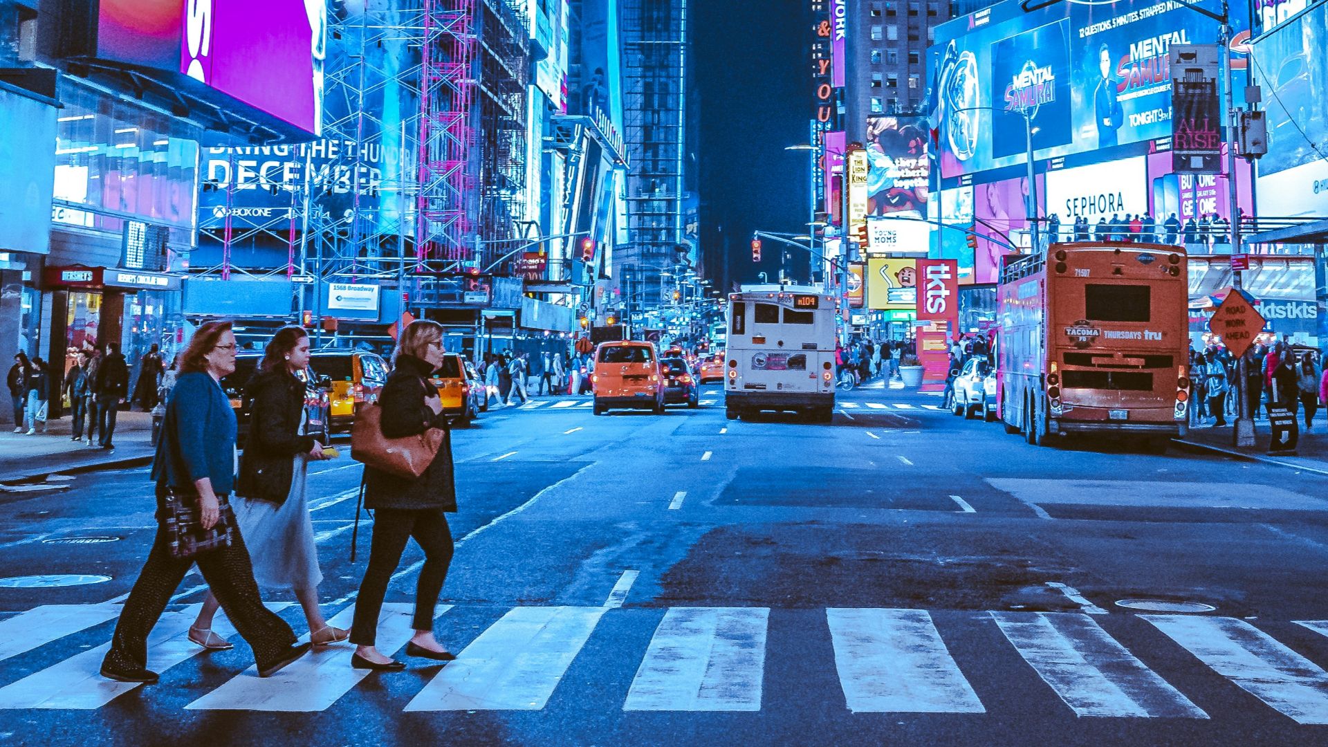 People crossing a street in Times Square, New York City, under bright neon signs