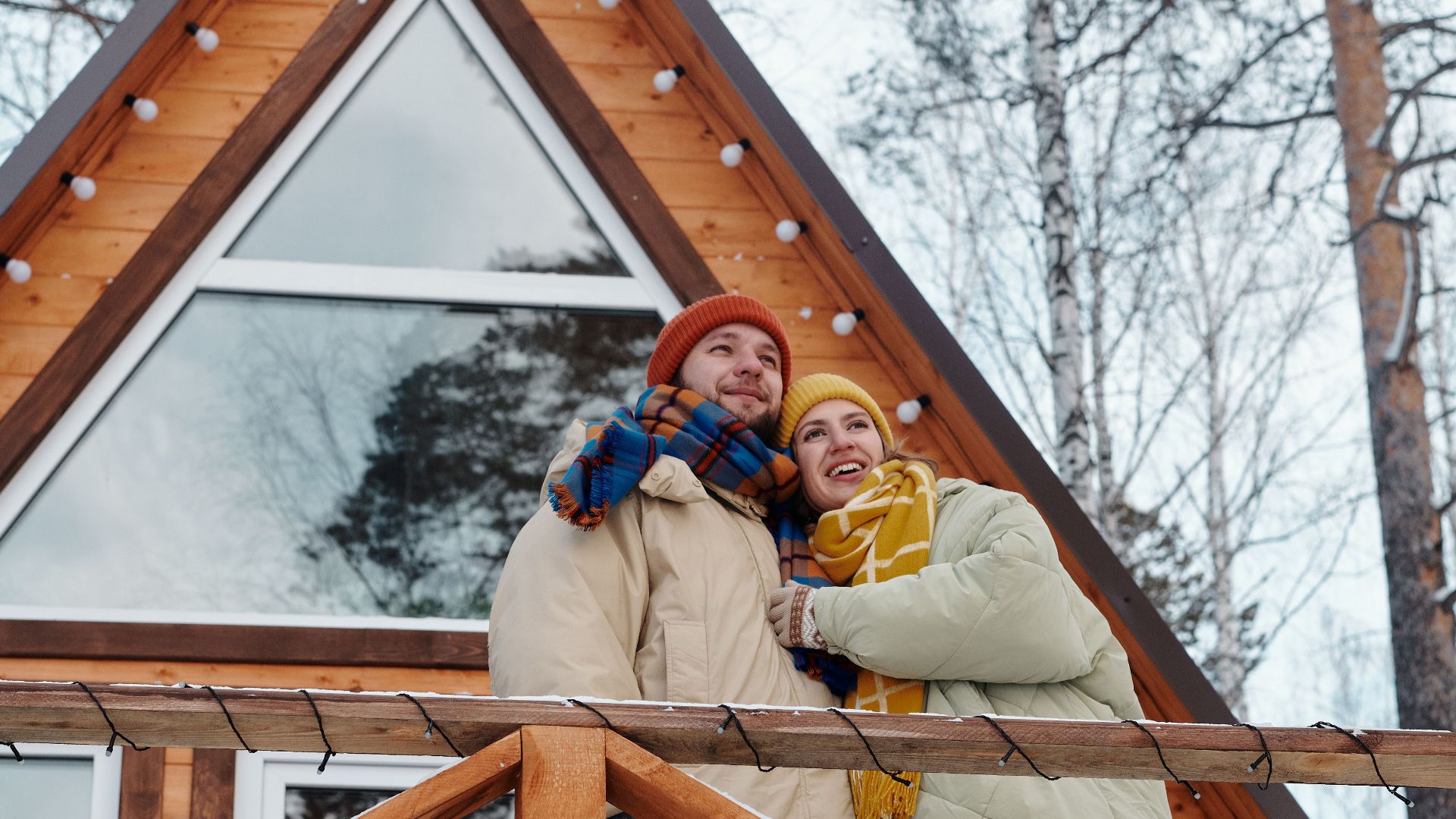 Couple with dog on cabin balcony in winter, enjoying nature.