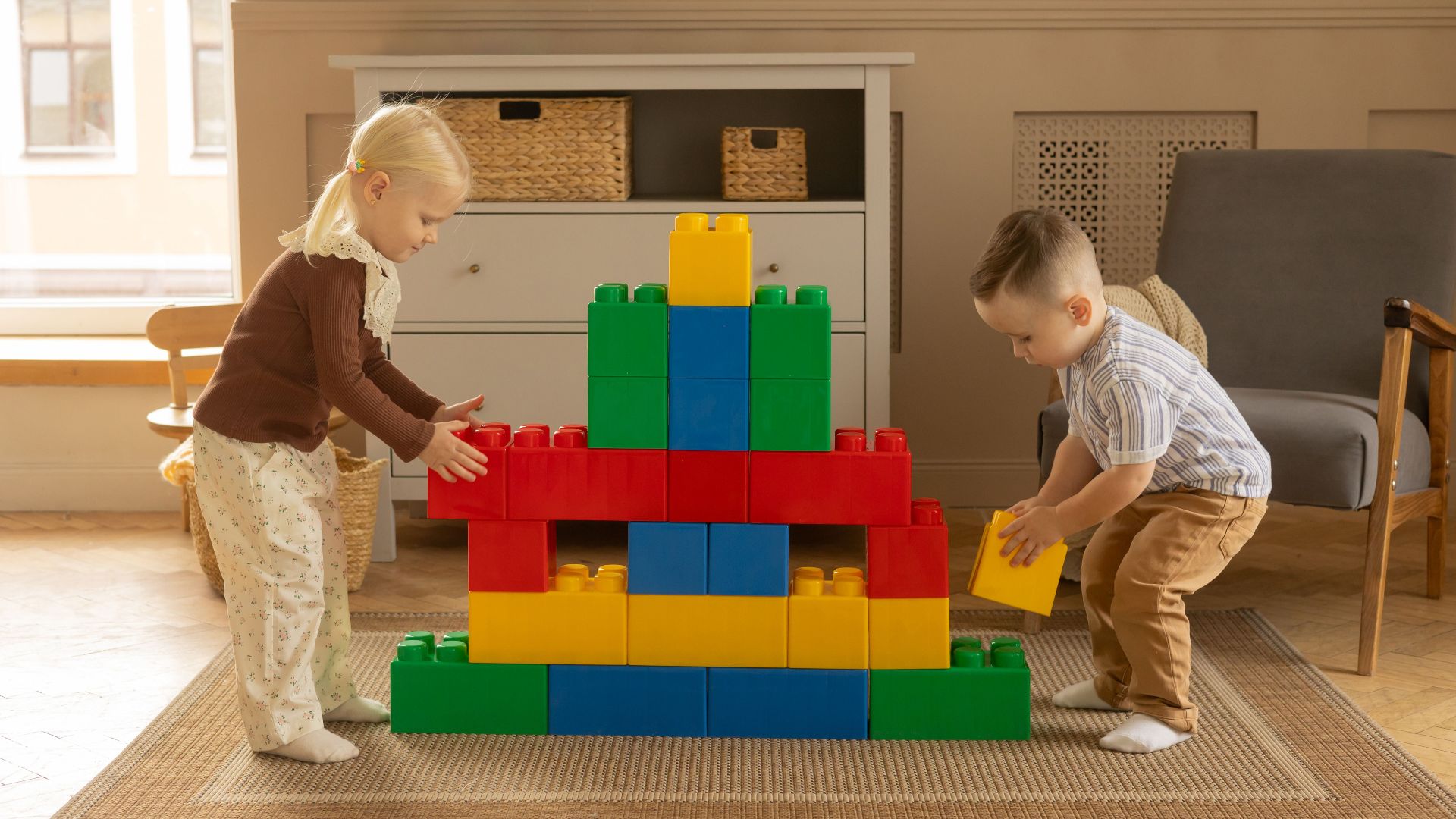 Two young children building with colorful blocks in a cozy living room setting.