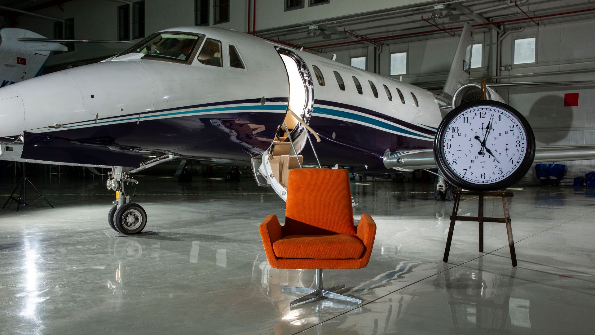 A private jet and modern furnishings inside an illuminated airport hangar.
