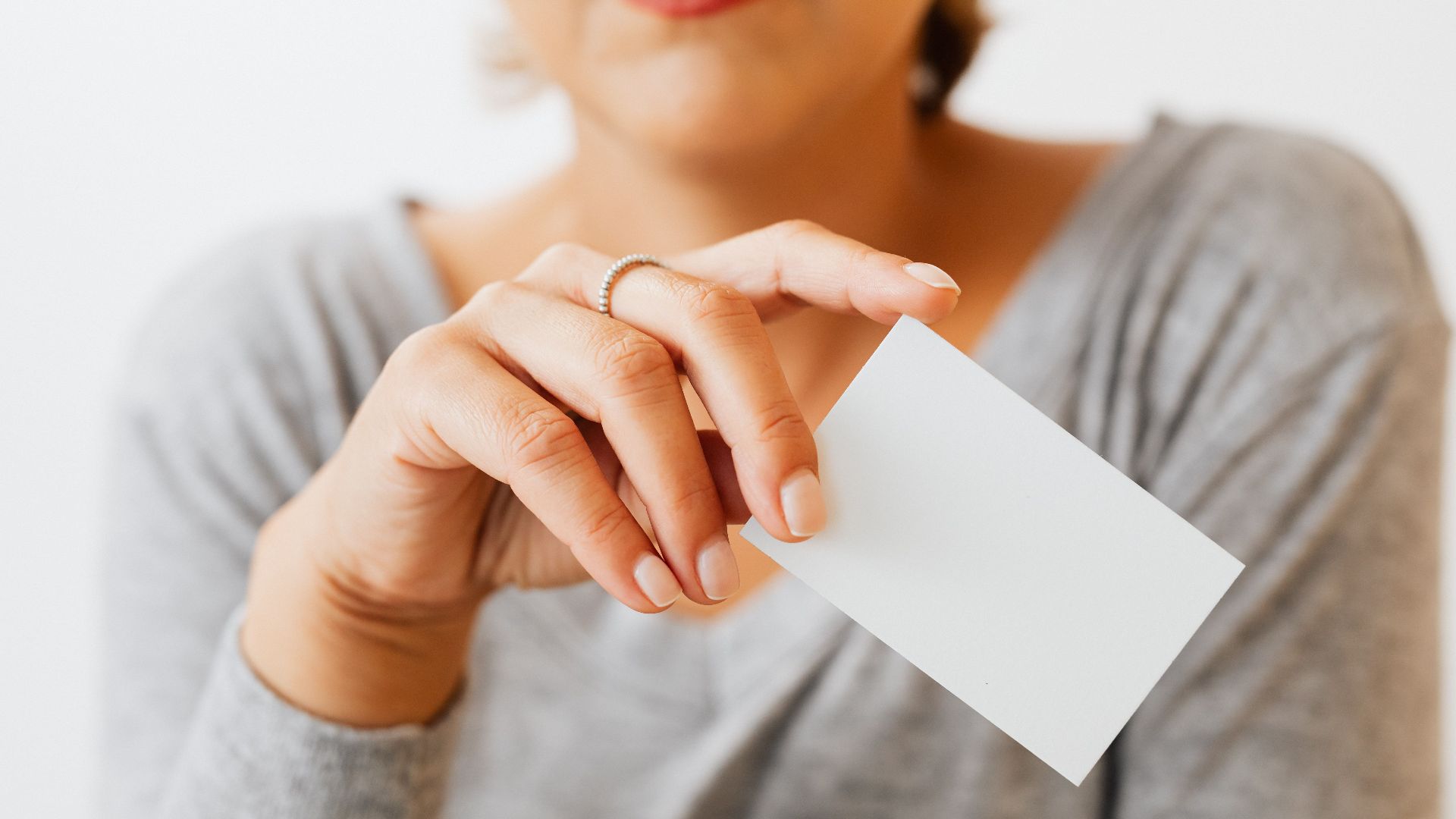 A woman in gray sleeves holding a blank business card, perfect for presentation or mockup use.